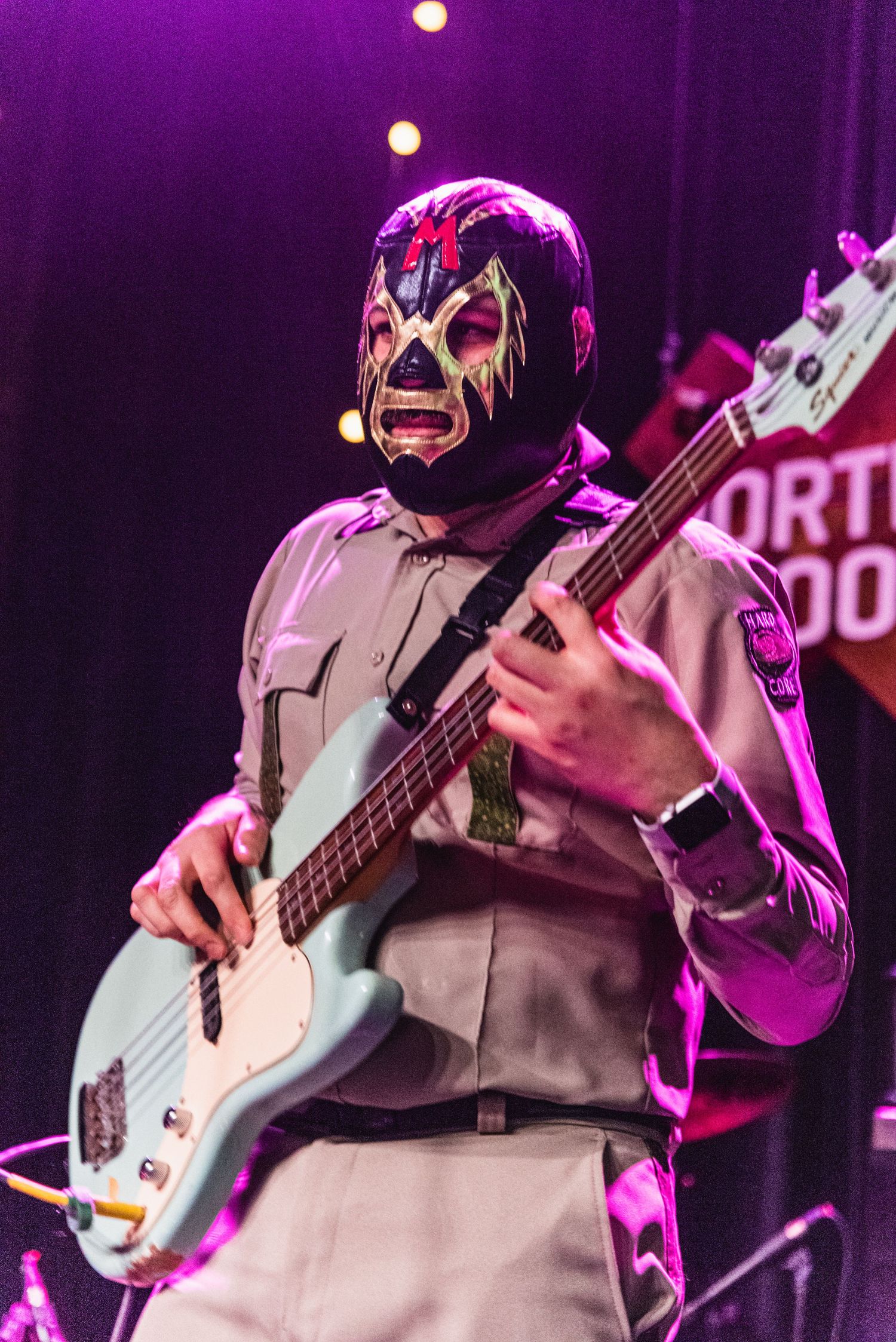 Musician in a wrestler mask plays bass guitar on stage under purple lighting at North Door venue.