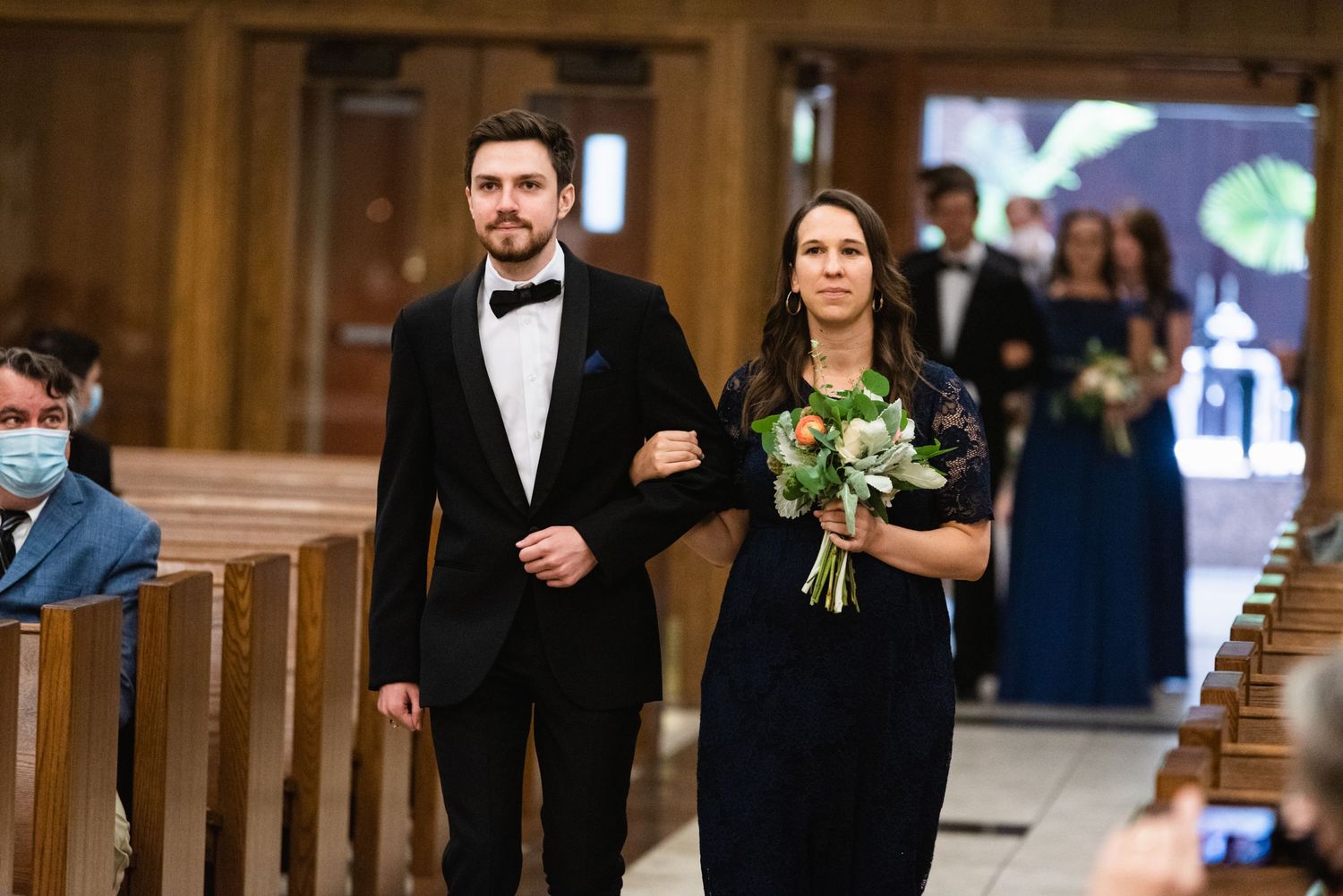Wedding party members walking down church aisle during ceremony processional.