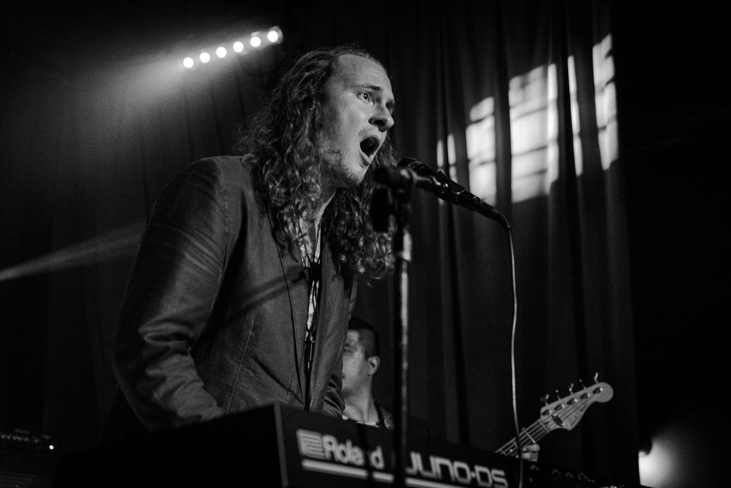 A performer passionately sings into a microphone on a dimly lit stage during a concert.