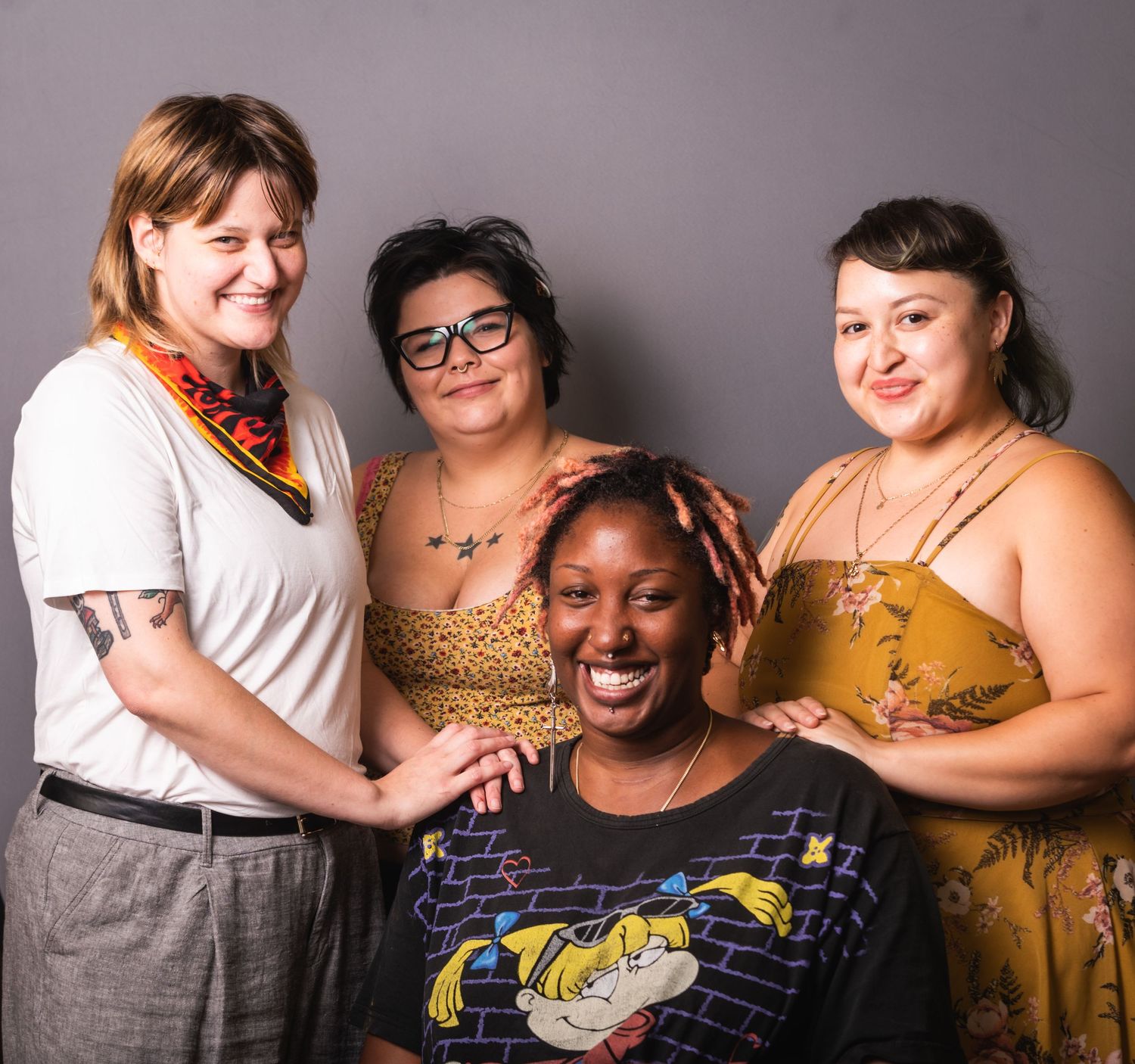 A diverse group of four friends smiling and posing together for a casual studio portrait.