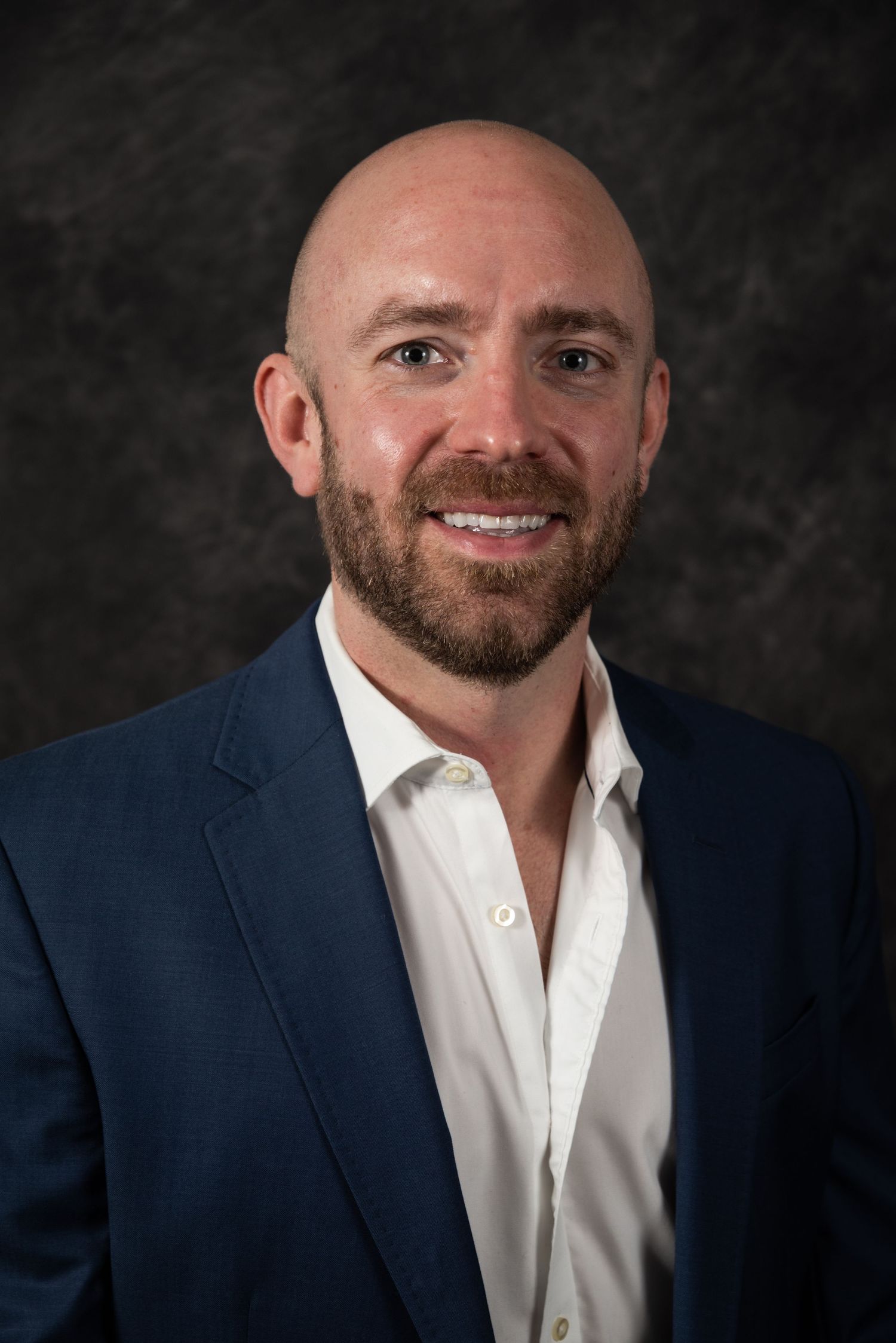 Executive headshot of person wearing navy blazer and white shirt with warm expression.