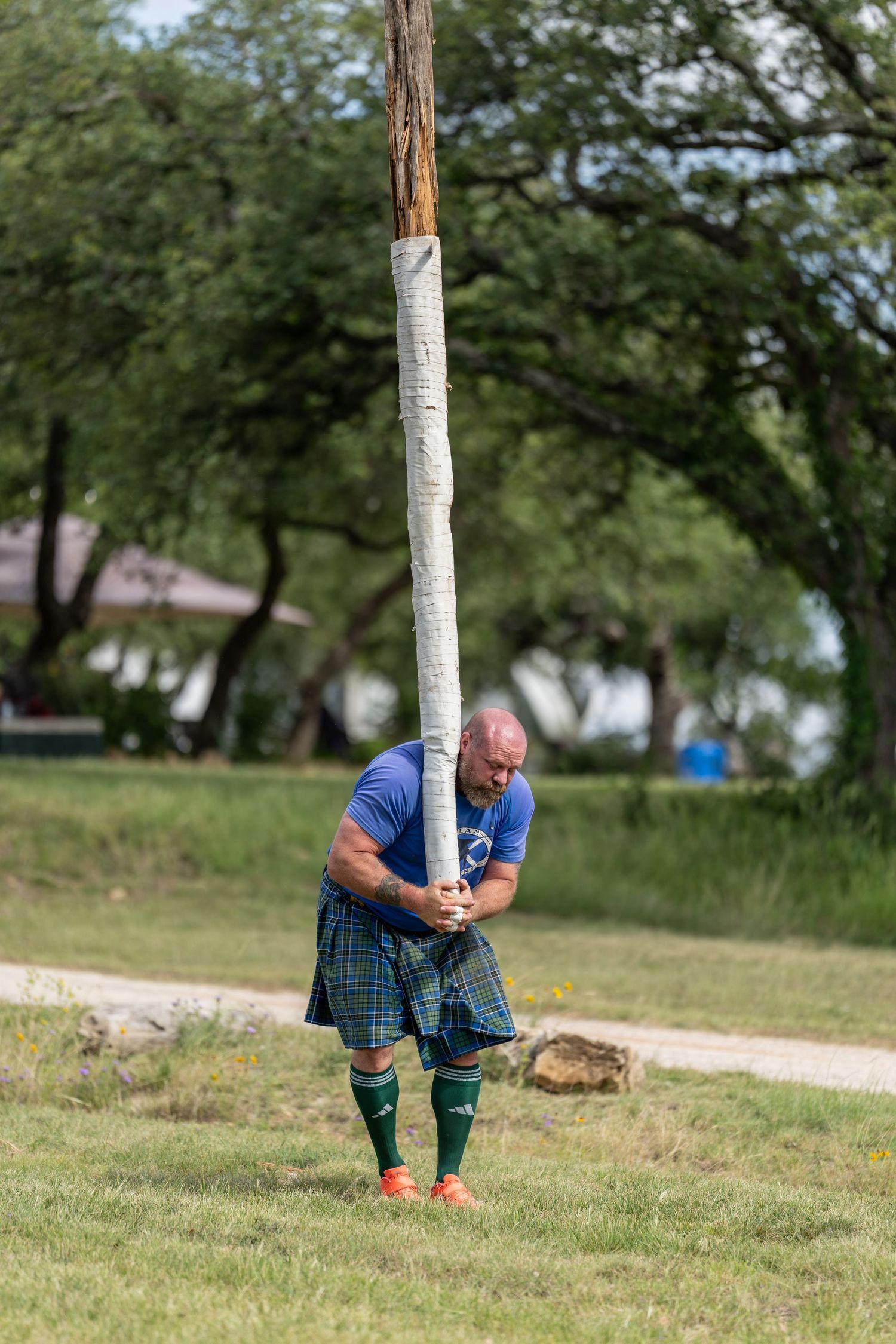 Man in blue shirt and tartan kilt tossing a caber at a Highland Games competition outdoors.