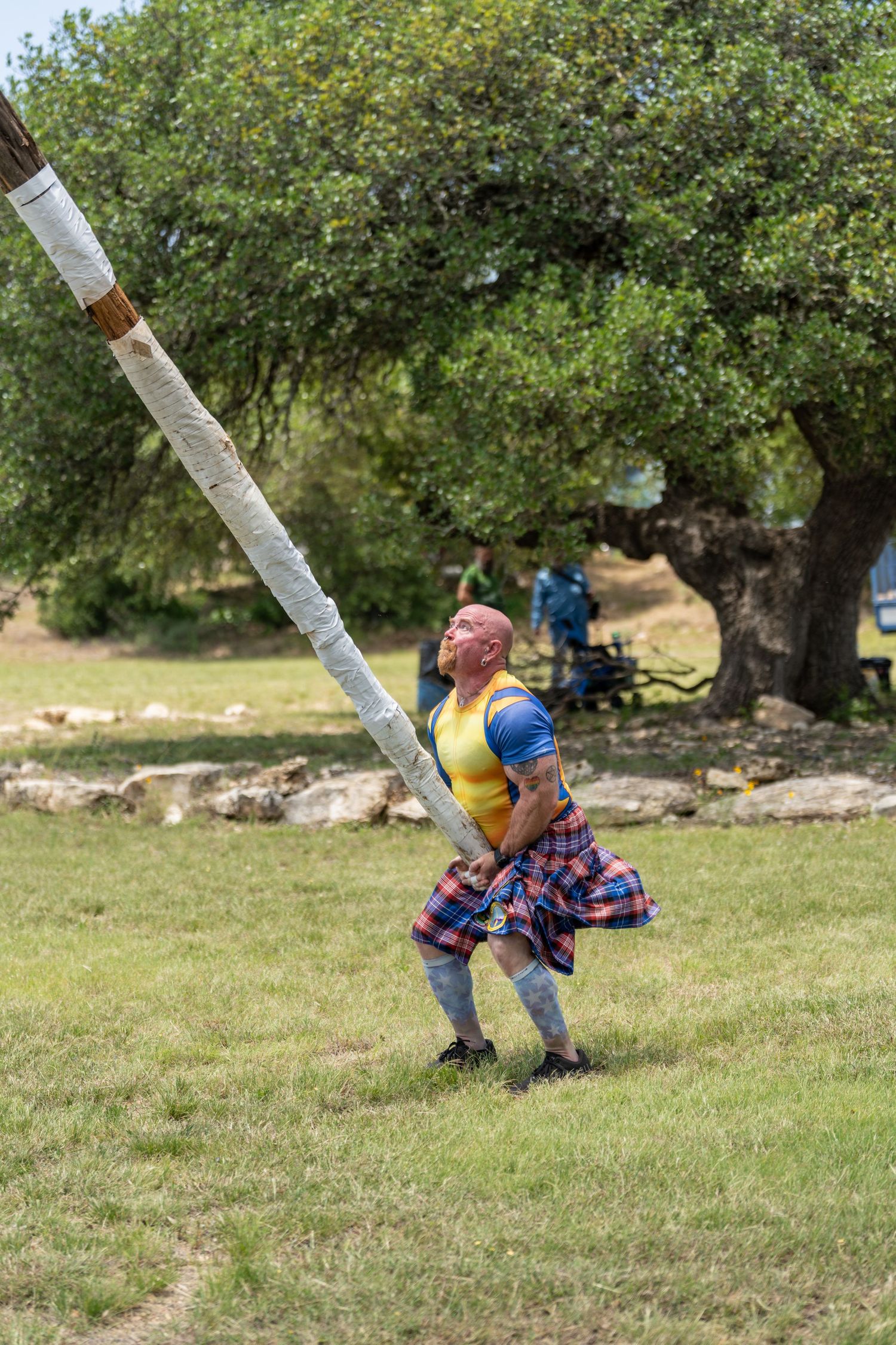 Man in tartan kilt tossing a caber at a Highland Games competition outdoors.