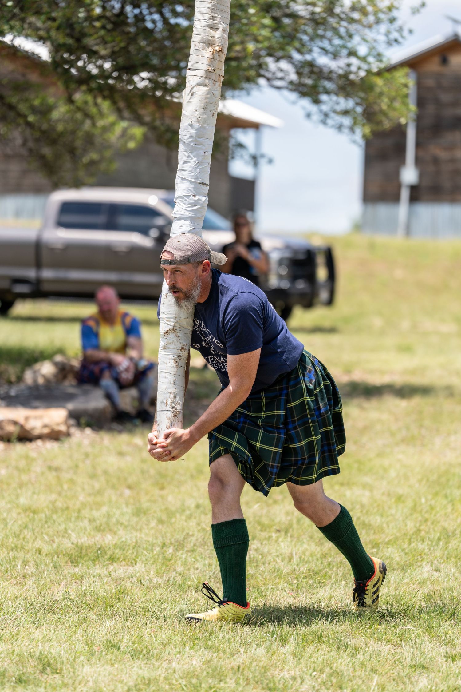 Man in tartan kilt tossing a caber at a Highland Games competition outdoors.