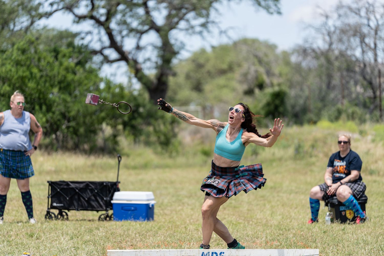 Woman competing in Highland Games throws event, wearing tartan skirt, with spectators watching in outdoor field.
