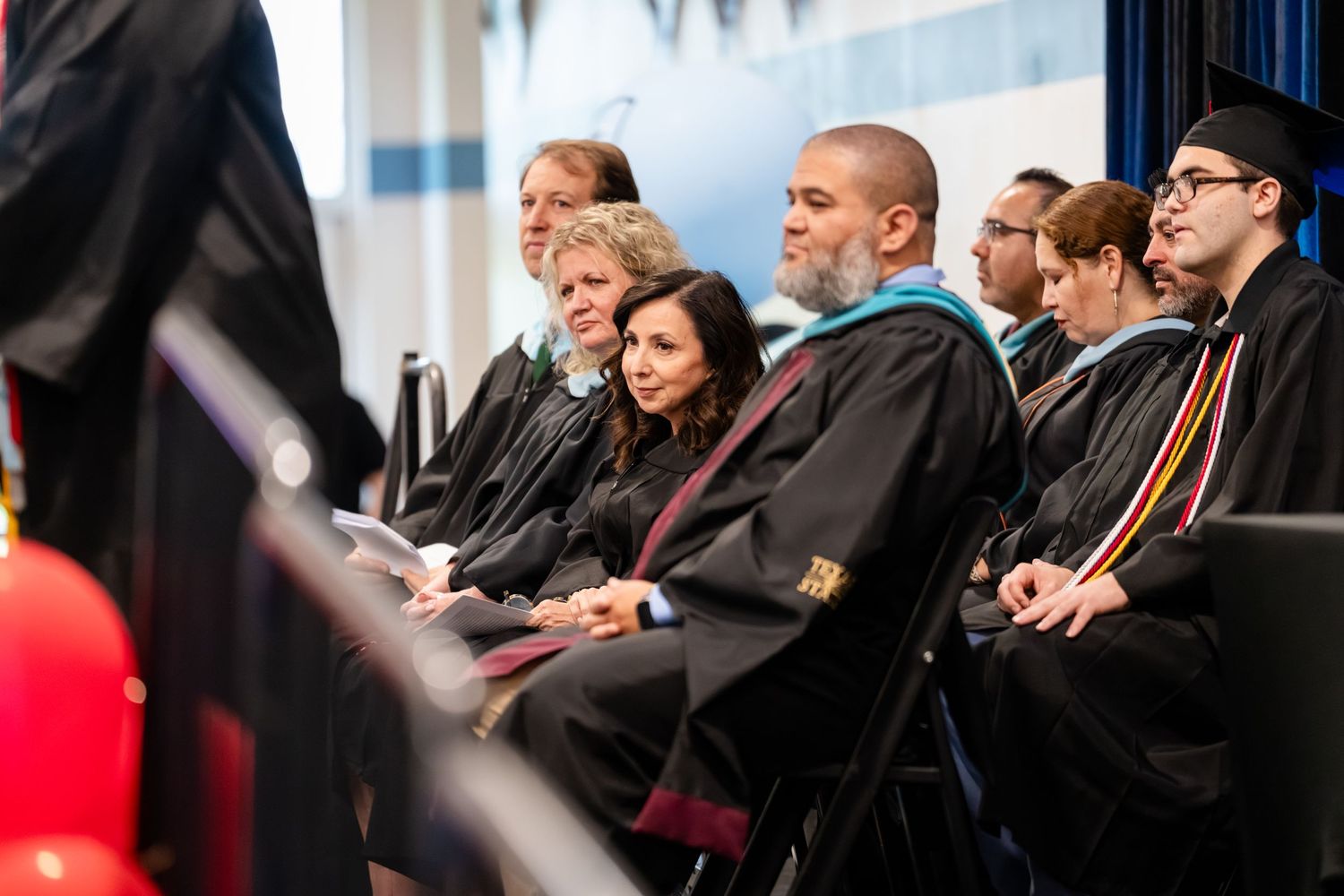 Group of academics in graduation gowns seated at a university commencement ceremony.