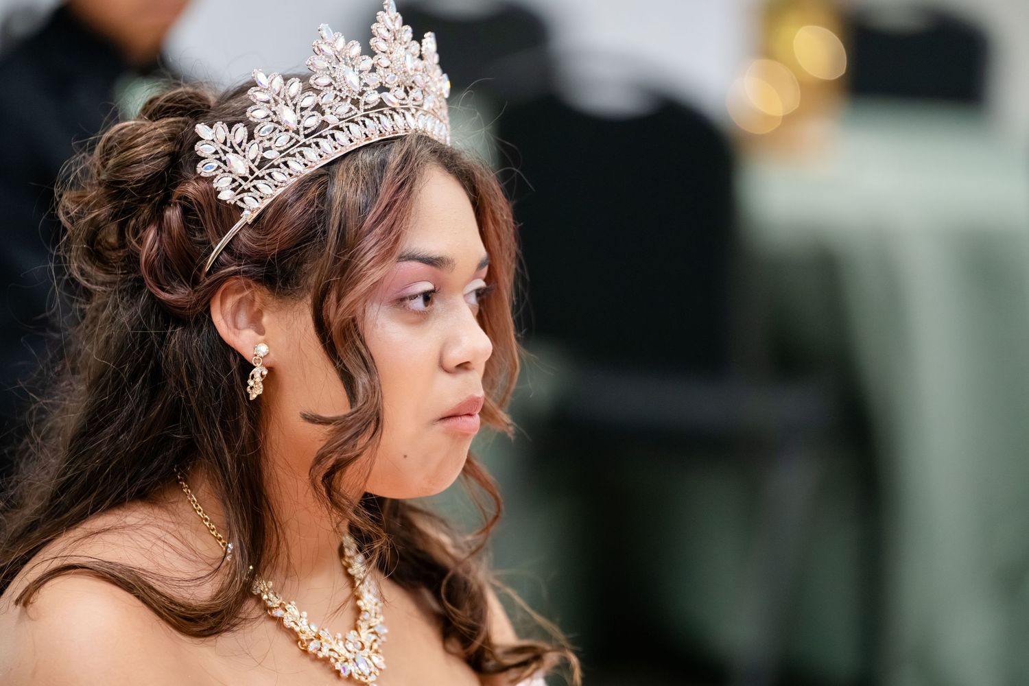 Young woman wearing a sparkling tiara and pearl jewelry at a quinceañera celebration.