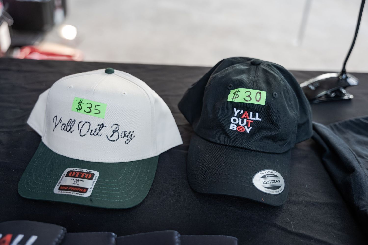 Two Fall Out Boy branded snapback hats displayed on a table, priced at $35 and $30 each.