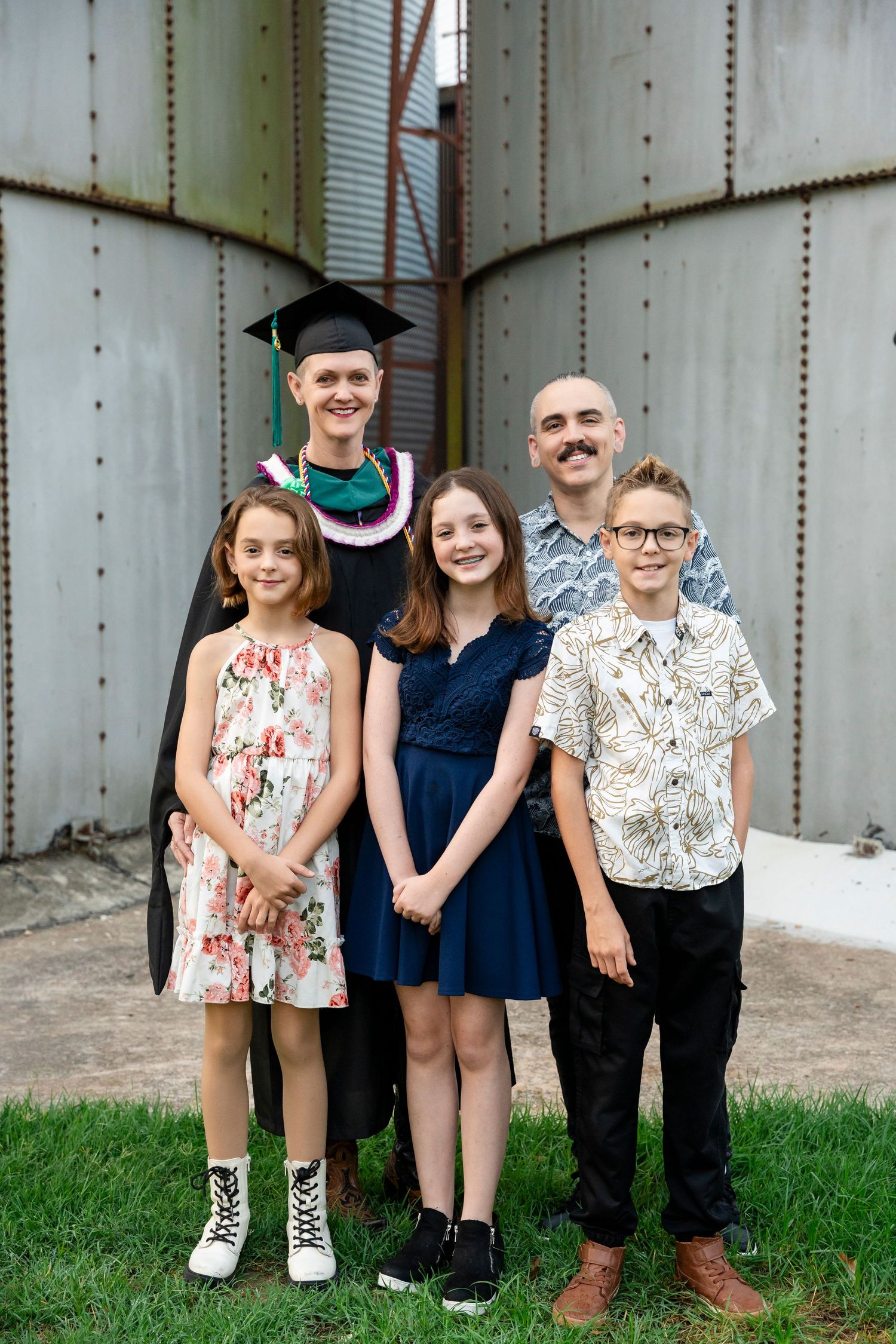 Family group poses together against industrial wall in casual attire with graduation cap.