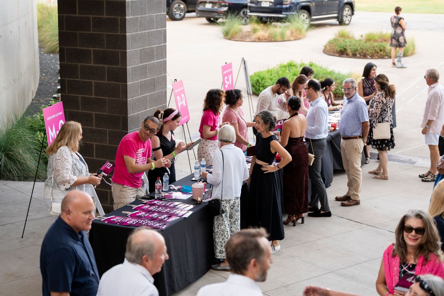 People gather at outdoor tables under a covered walkway during a social event or gathering.
