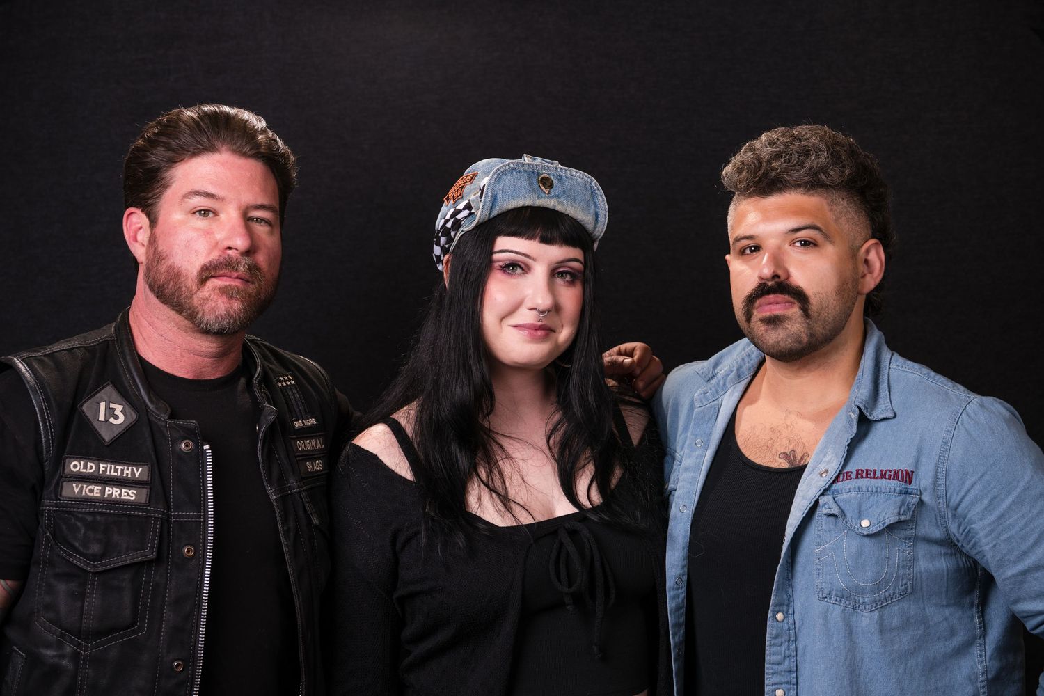 Three people in casual attire pose together against a black background for a portrait photo.