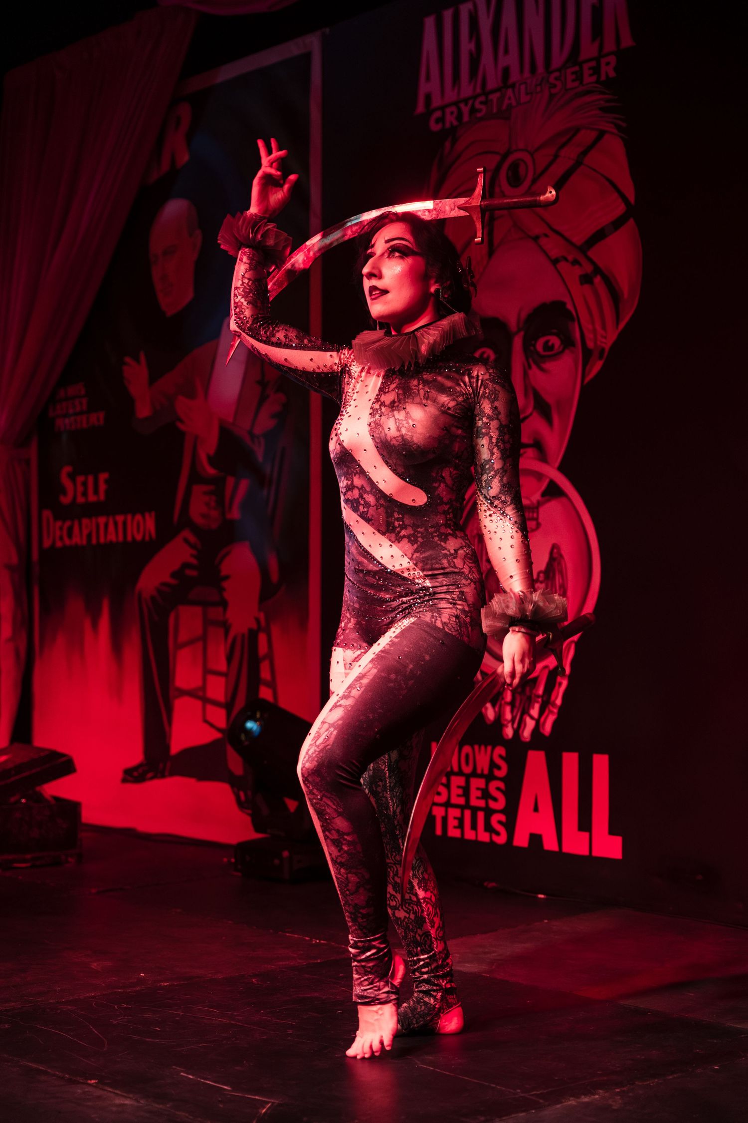 A dancer performs energetically in a red-lit venue wearing a sparkly outfit during a theatrical performance.