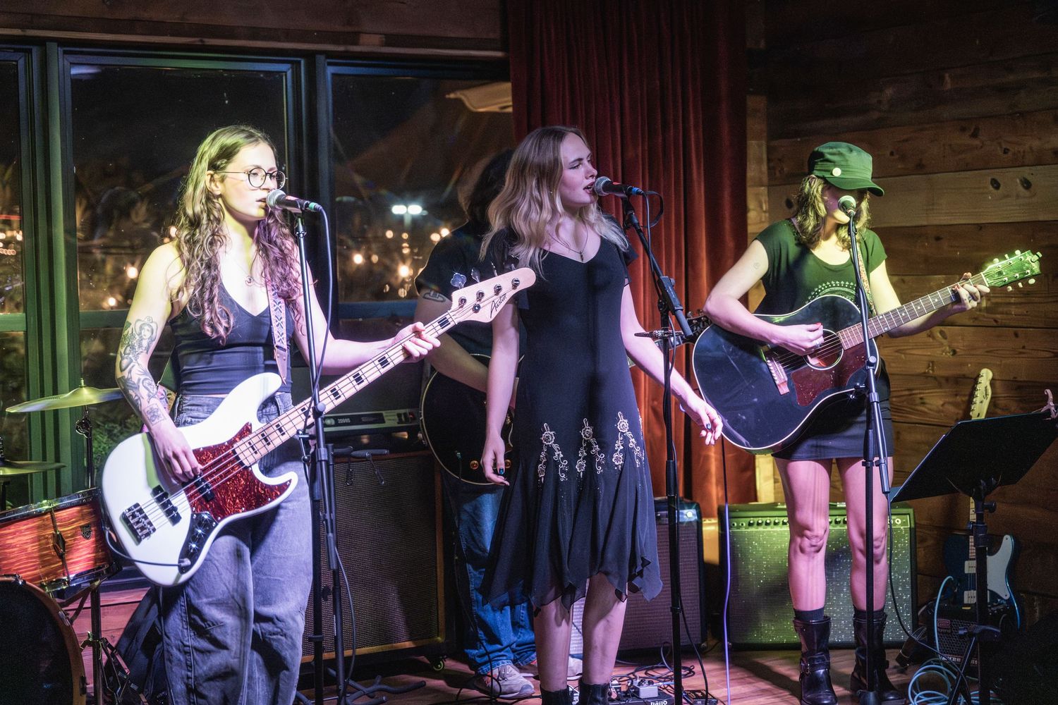 Musicians perform on stage with guitars and microphones at a dimly lit live music venue.