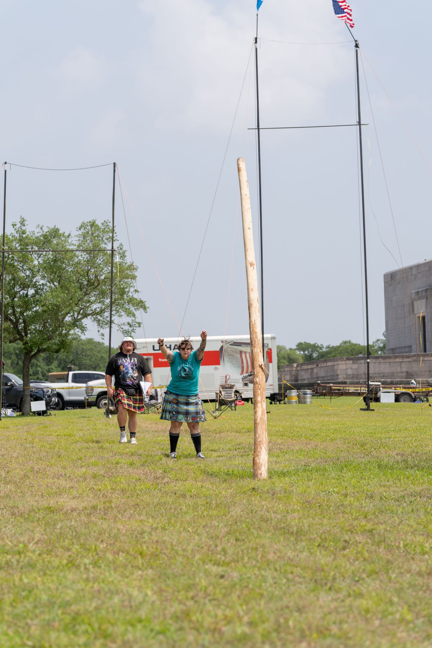 Two athletes in kilts compete in a caber toss event at an outdoor Scottish Highland Games competition.