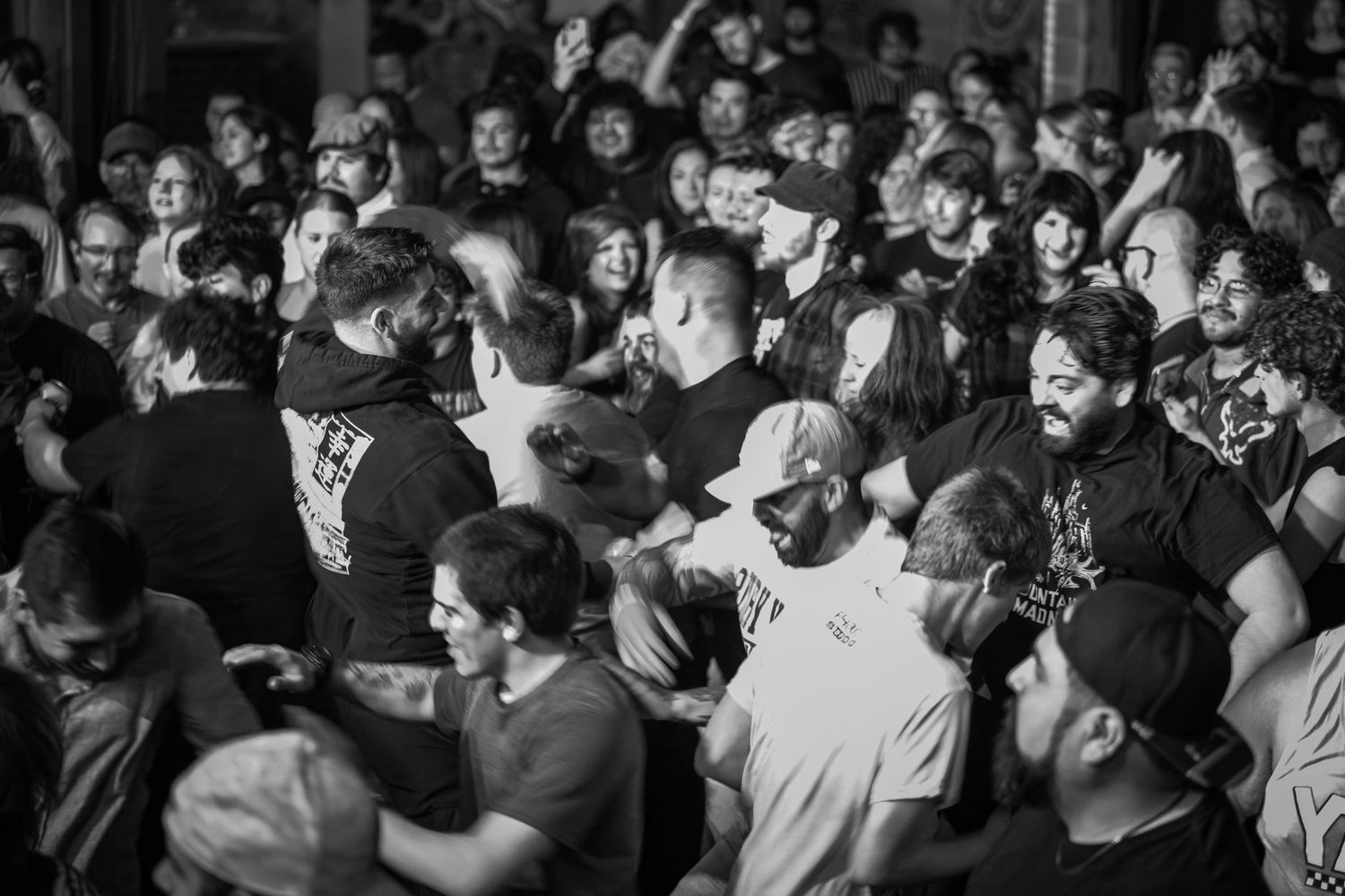 Black and white photo of a dense crowd at a live punk rock concert, with fans moshing and engaging in the pit.