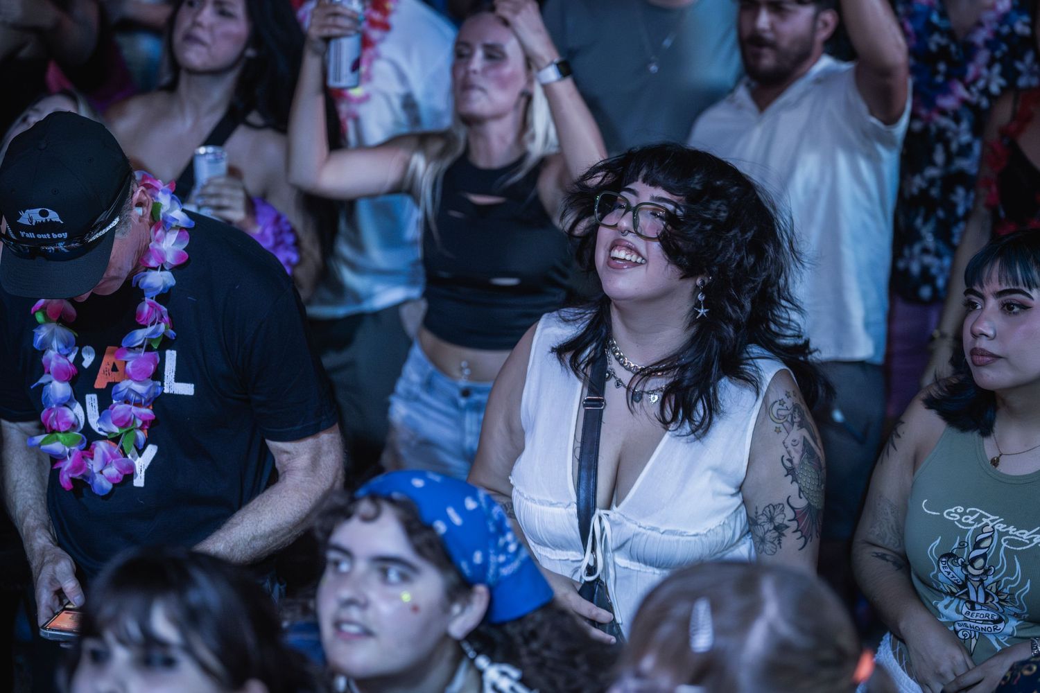 Concert crowd cheers and dances enthusiastically at a live music performance in a dark venue.