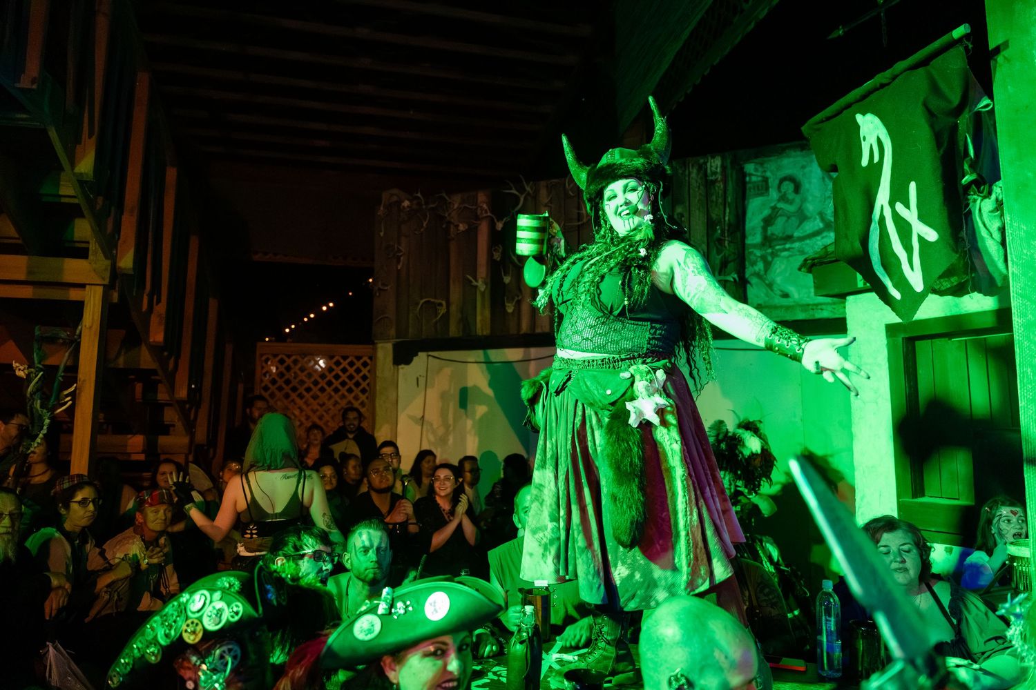 A theatrical performance illuminated in bright green lighting shows performers on stage during a dramatic scene.
