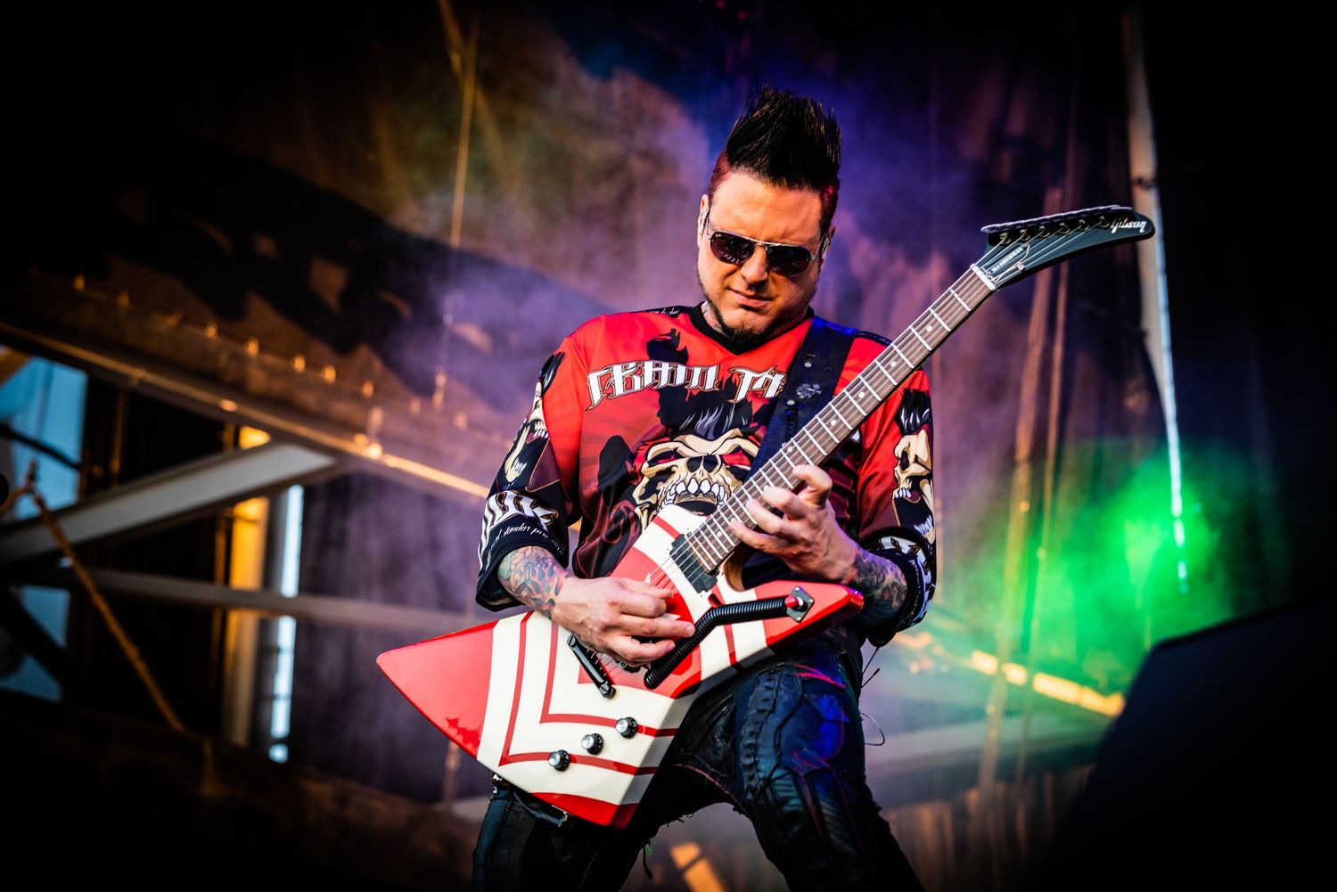 A guitarist performs on stage under colorful lighting during a live concert performance.