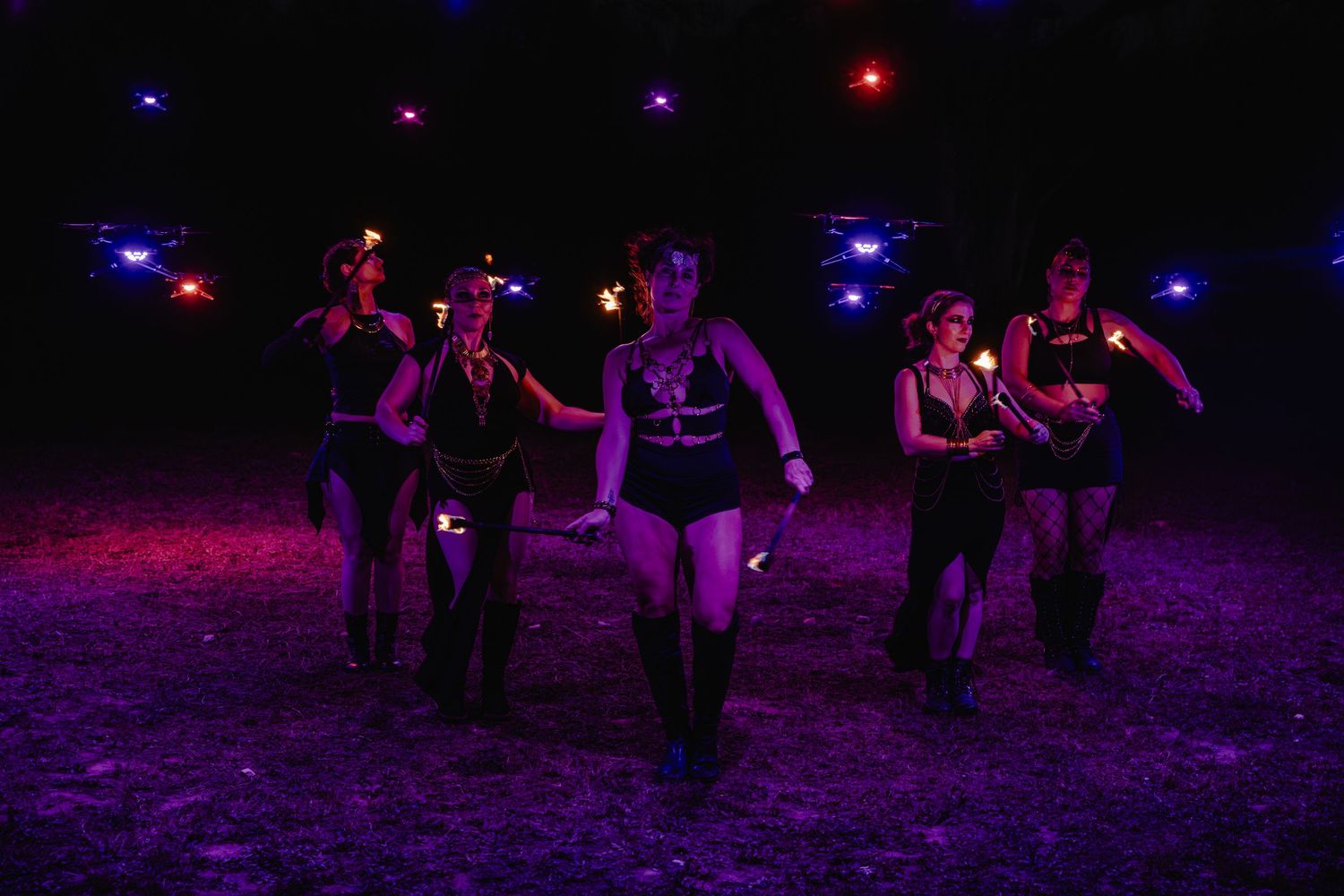 Performers dancing on a dark stage illuminated by colorful purple and red lights during a show.