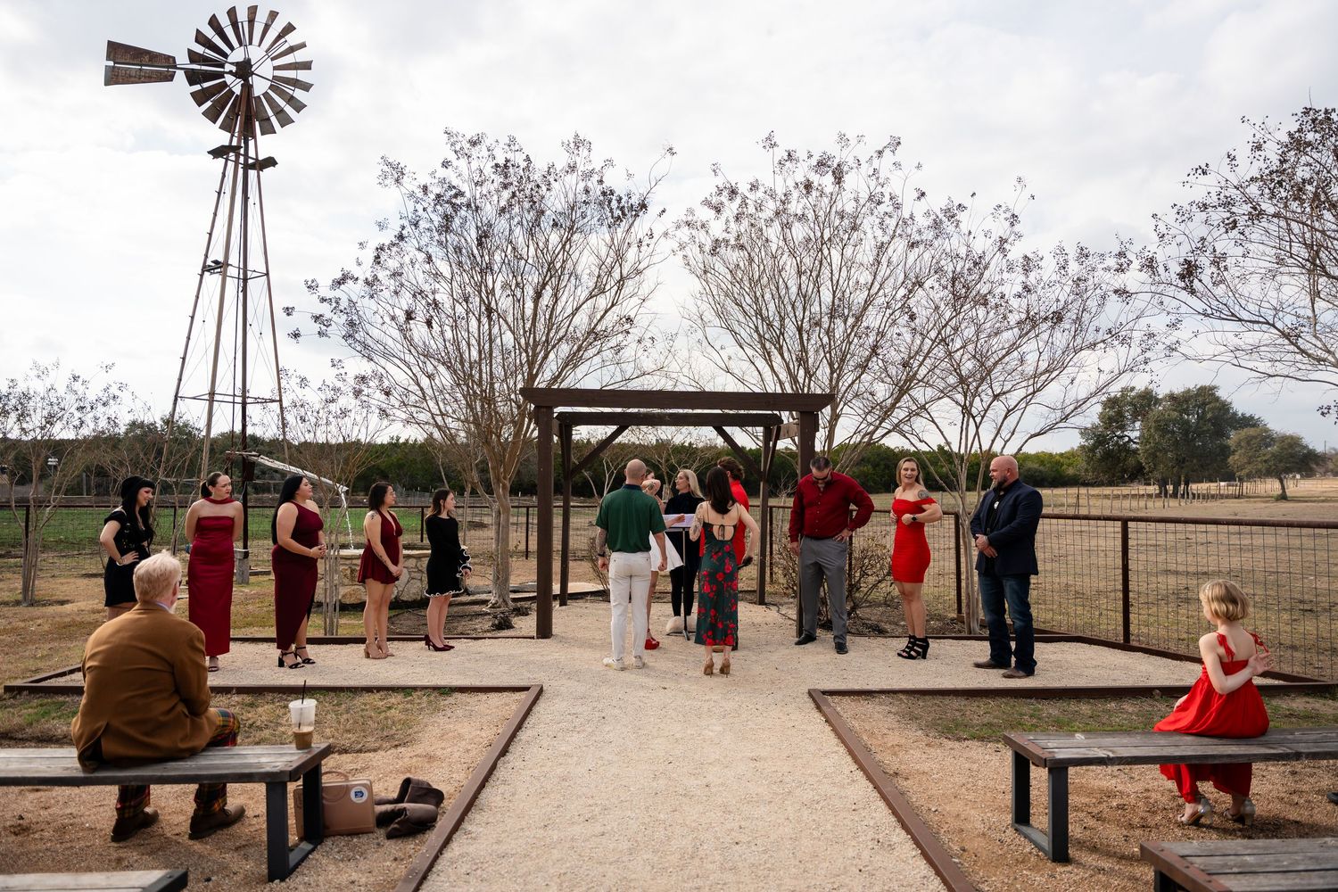 Outdoor wedding ceremony near a windmill with guests in red and black attire gathered on a rustic ranch venue.
