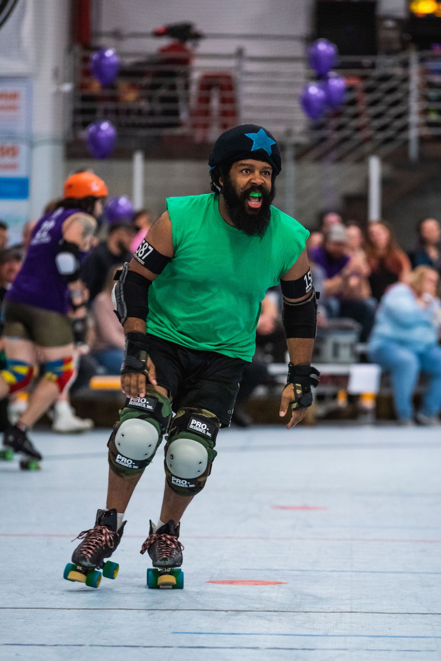 Roller derby athlete in green shirt and protective gear skates on indoor rink.