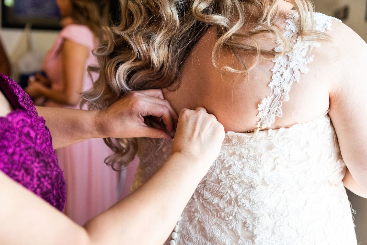 Close-up of wedding dress being buttoned up during bridal preparations.