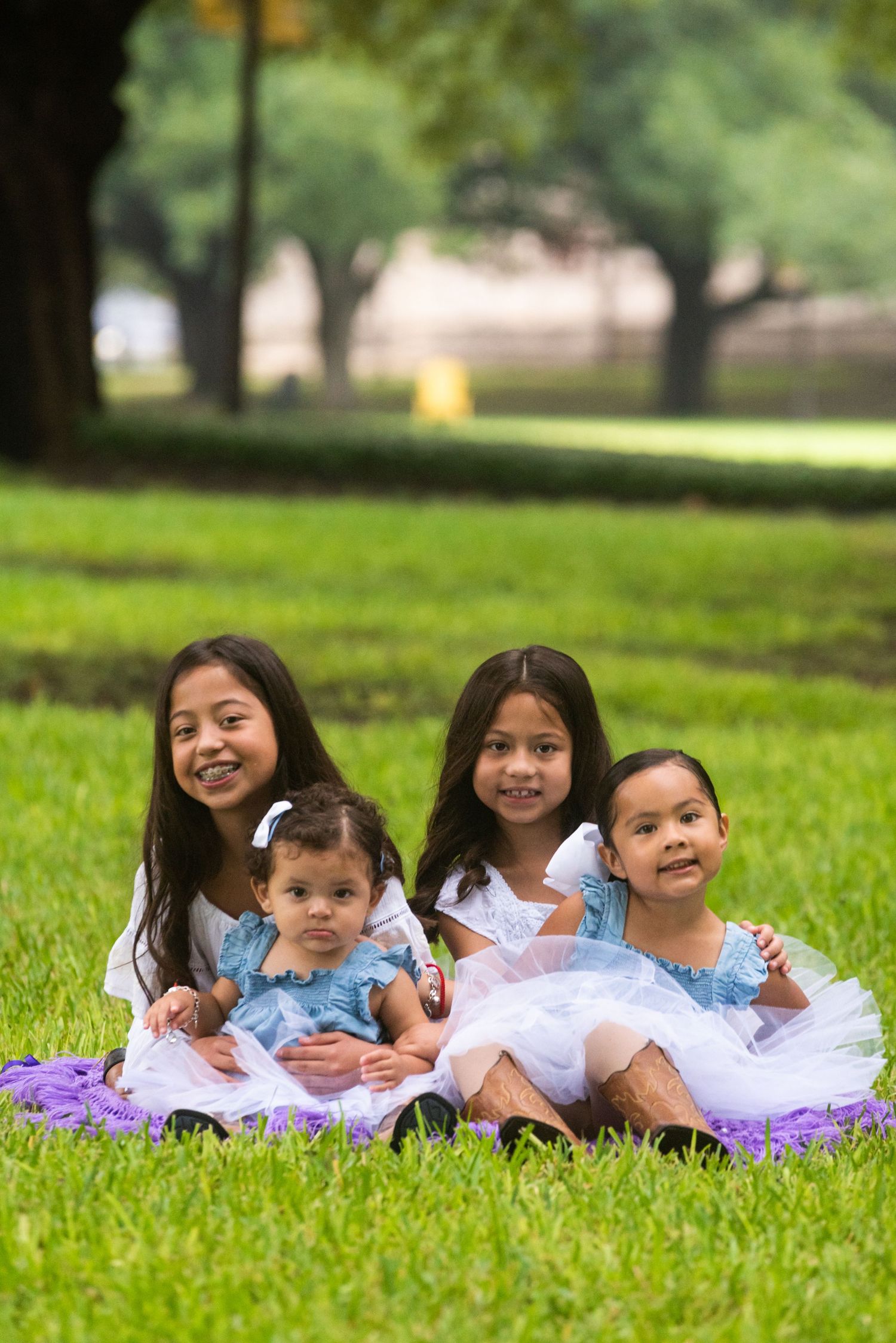 A family group sits together on green grass wearing coordinated blue and white outfits.