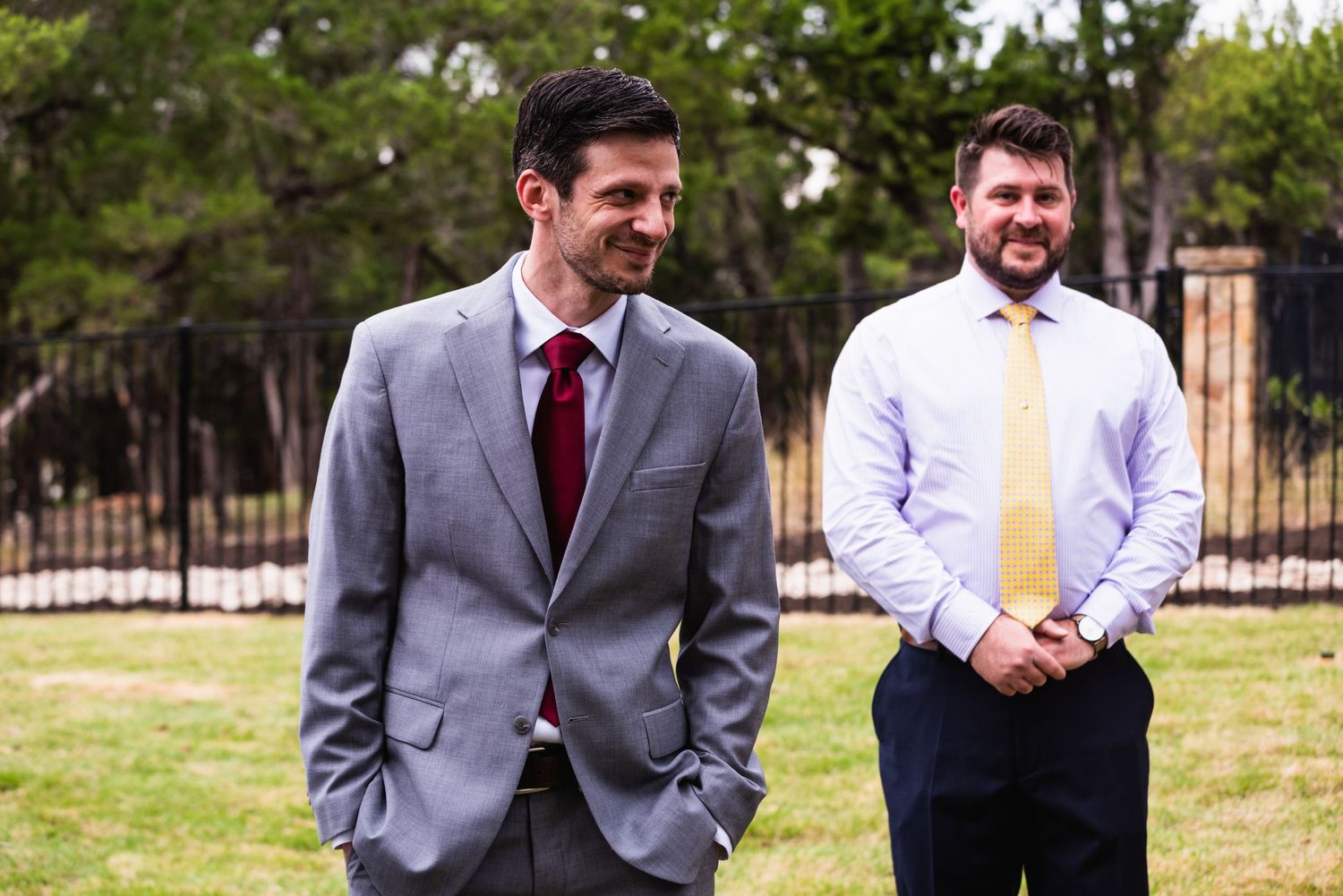 Two men in formal attire share a laugh on grassy lawn.