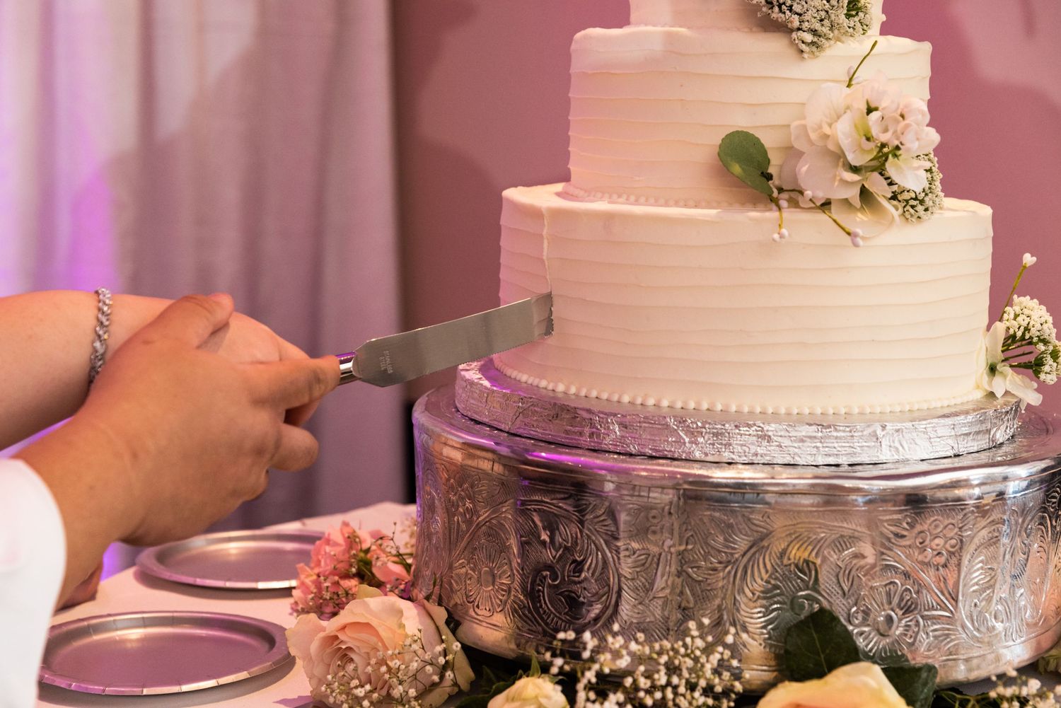 Close-up of hands cutting into a white tiered wedding cake with floral decorations.