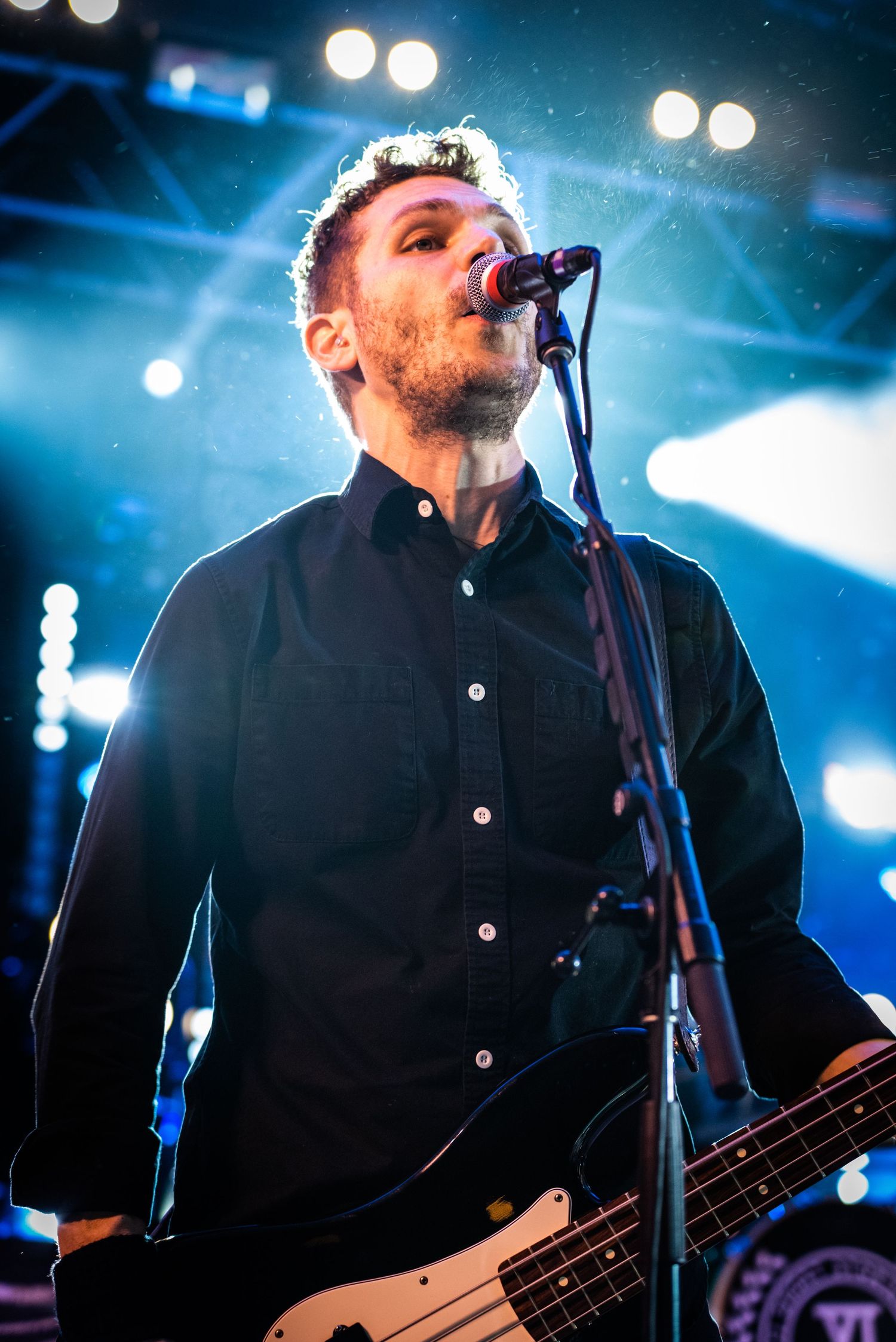 Performer sings into microphone on stage with dramatic blue lighting and smoke effects.