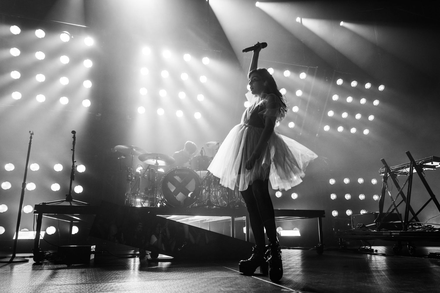 Silhouetted performer on stage with dramatic backlighting and bright spotlights creating an ethereal atmosphere.