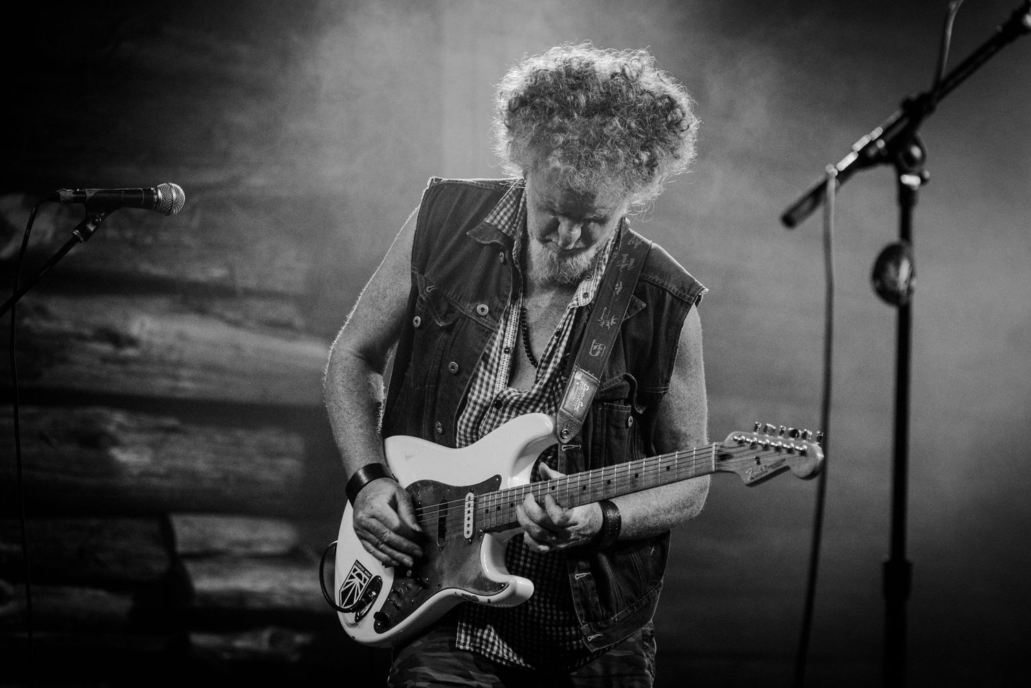 Musician plays white electric guitar during moody black and white stage performance.