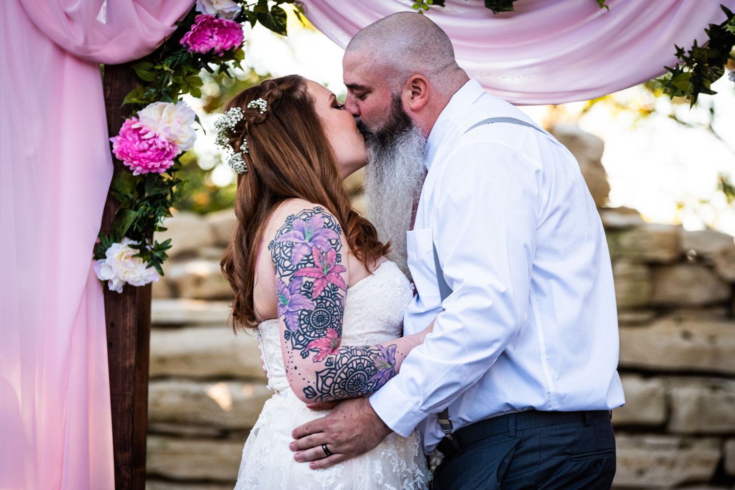 A romantic moment under a pink floral arch with roses and draped fabric.