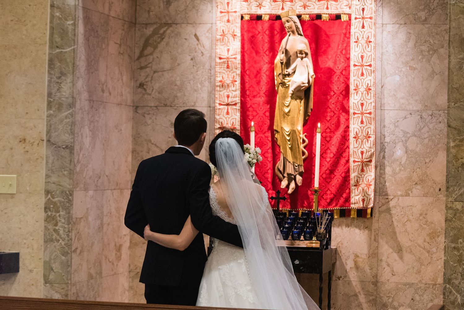 Bride and groom observe religious artwork on red banner during church ceremony.