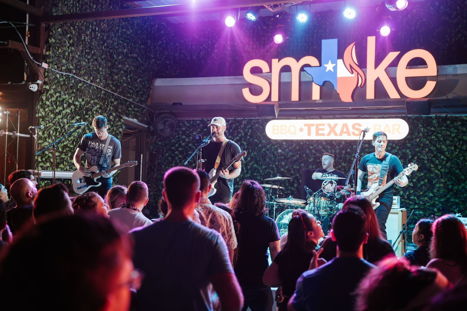 Rock band performing on stage under colorful lights with illuminated Smoke venue sign.