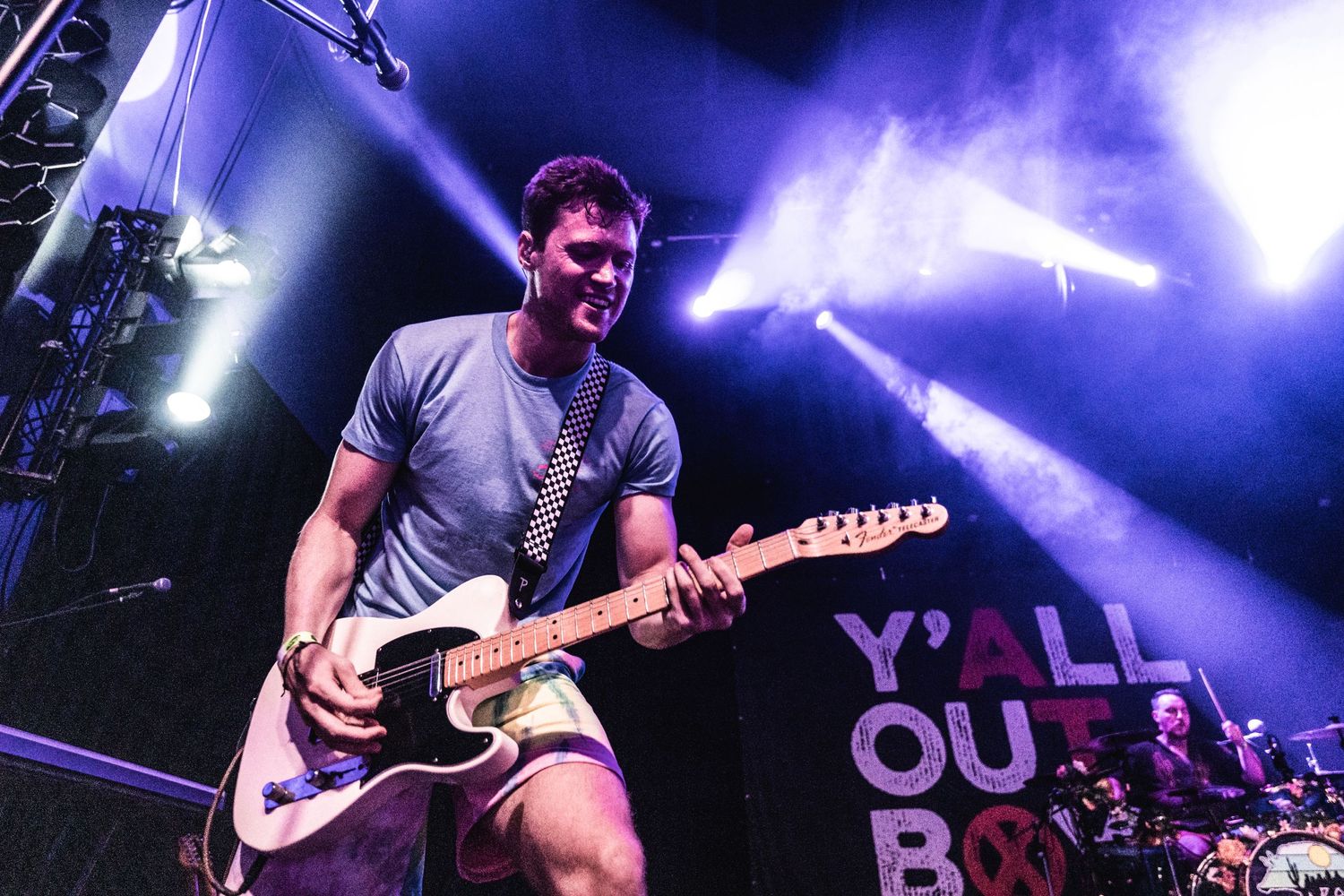 Guitarist performs on stage with dramatic purple lighting and 