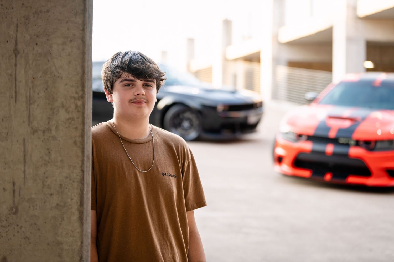 A portrait beside customized performance cars in an urban parking structure.
