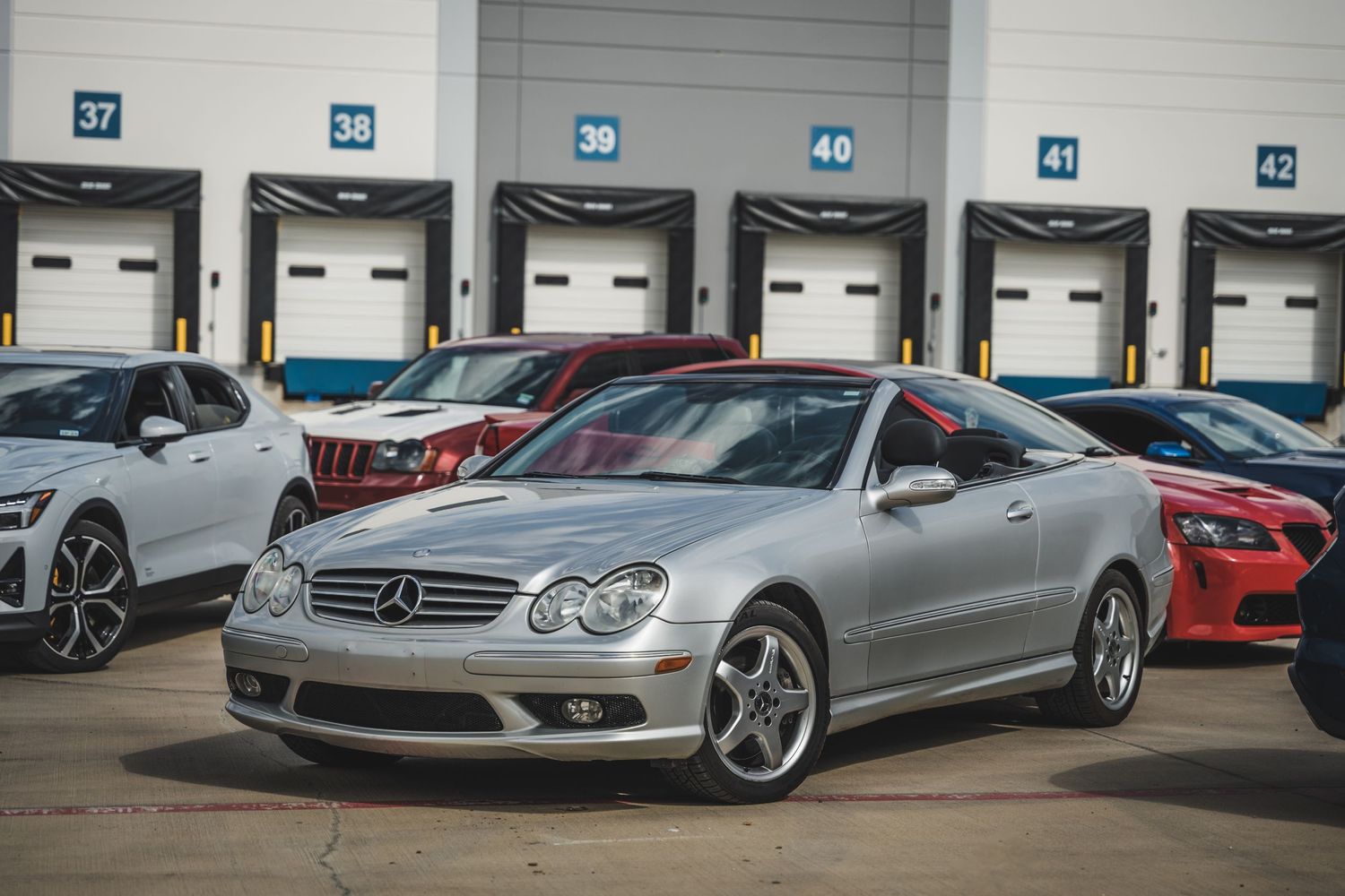 Silver Mercedes-Benz CLK with sport wheels positioned in front of industrial warehouse bays.