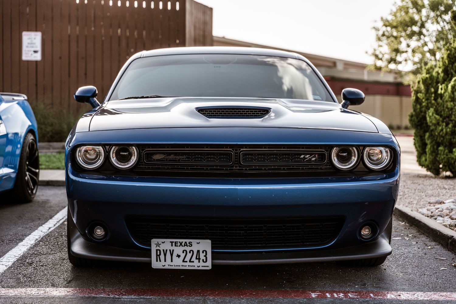 Front view of a blue Dodge Challenger with glowing LED headlights in a parking lot.