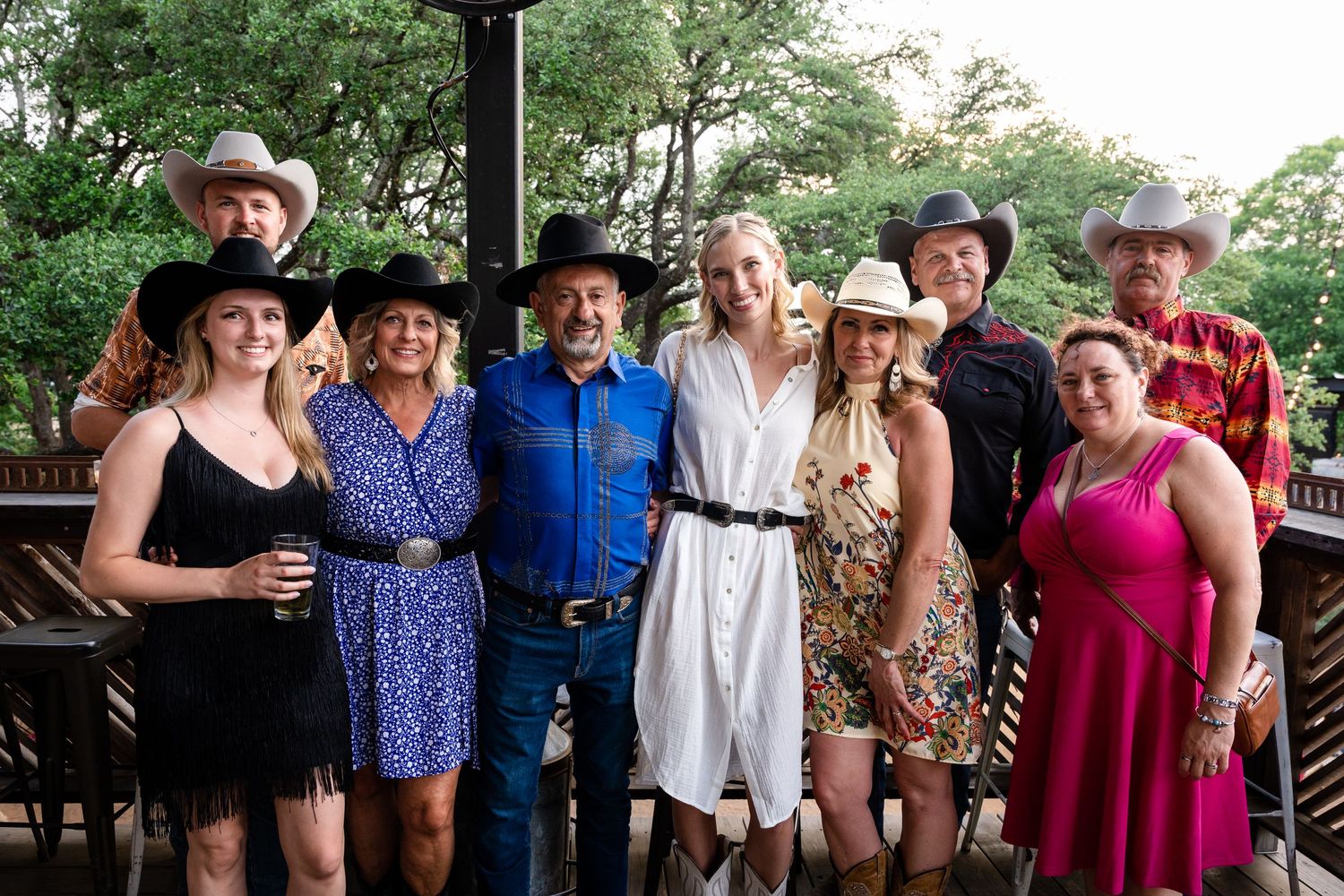 Group photo of wedding guests in western attire on outdoor deck.