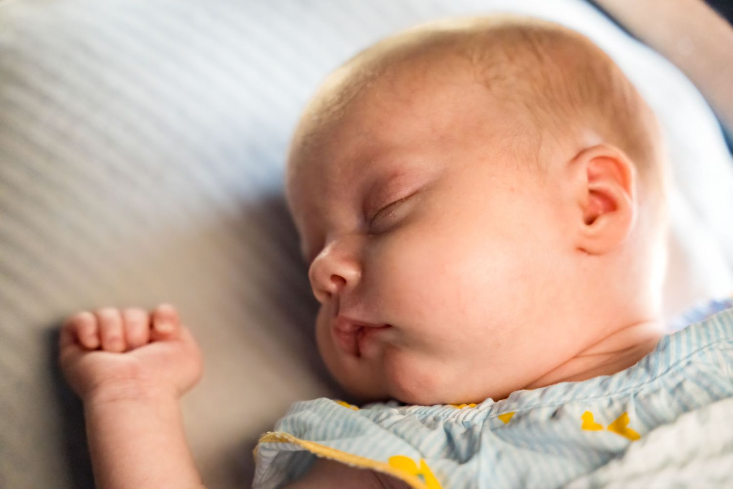 Peaceful sleeping baby in close-up with tiny fist raised against white bedding.