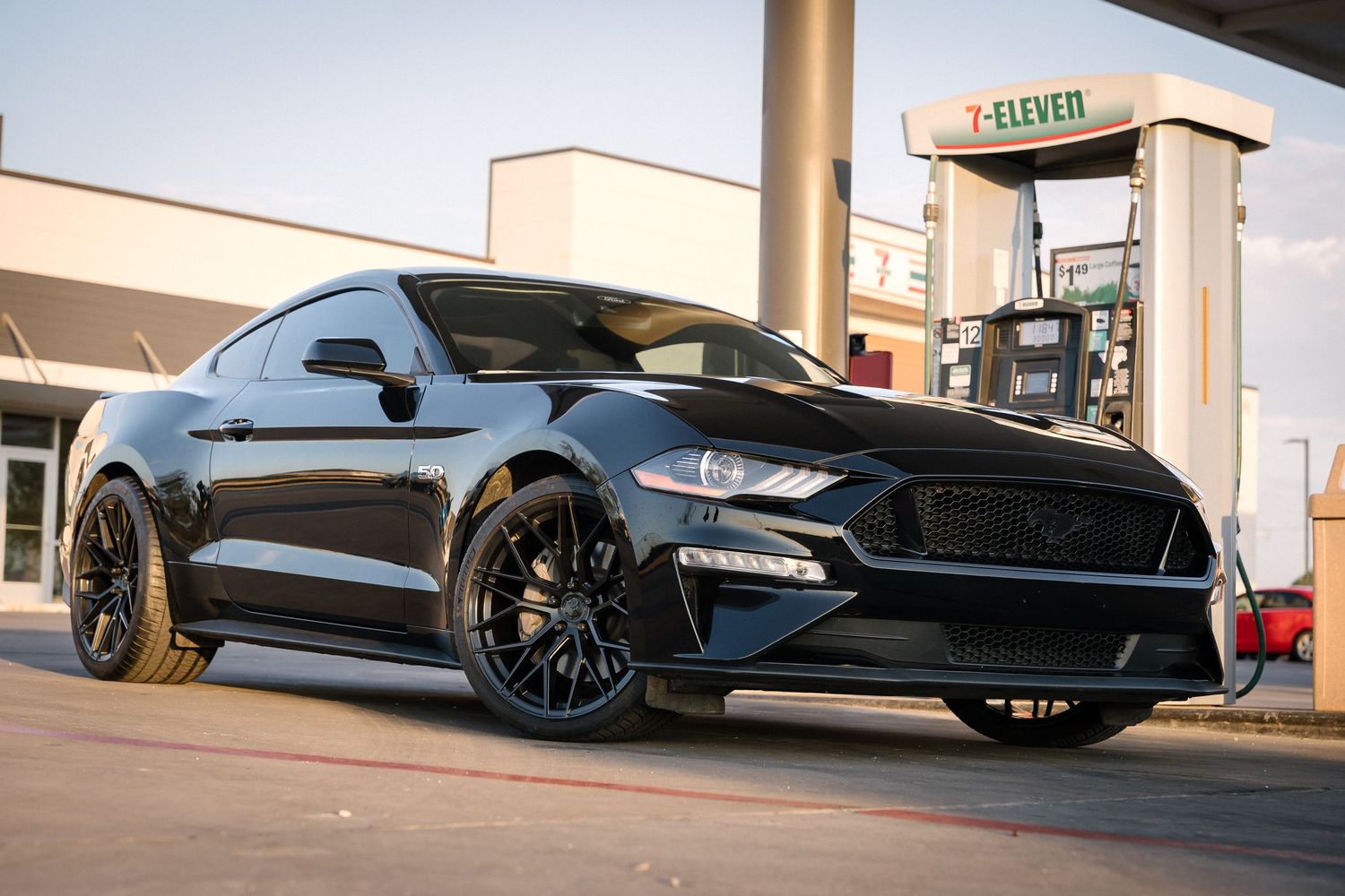 Black Ford Mustang with custom black wheels parked at gas station.