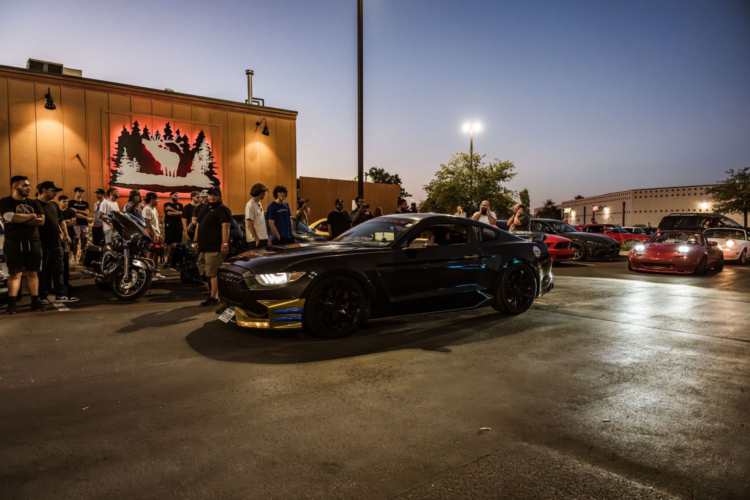 Custom black sports car parked at night outside building with crowd gathering.