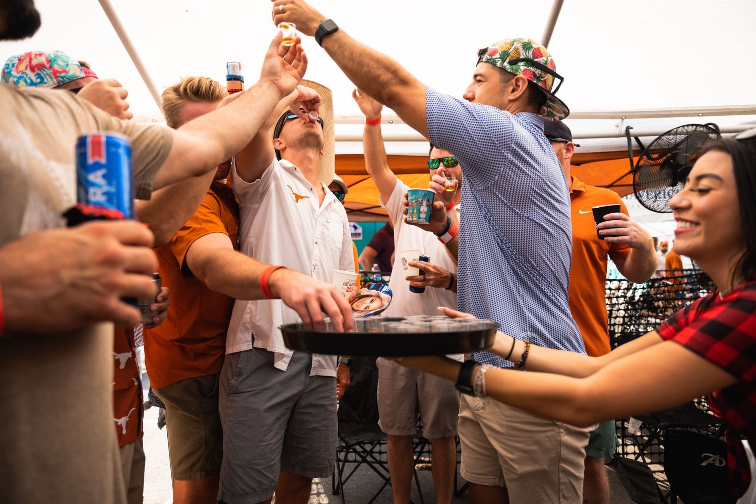 Party crowd with raised arms cheering during an outdoor celebration.