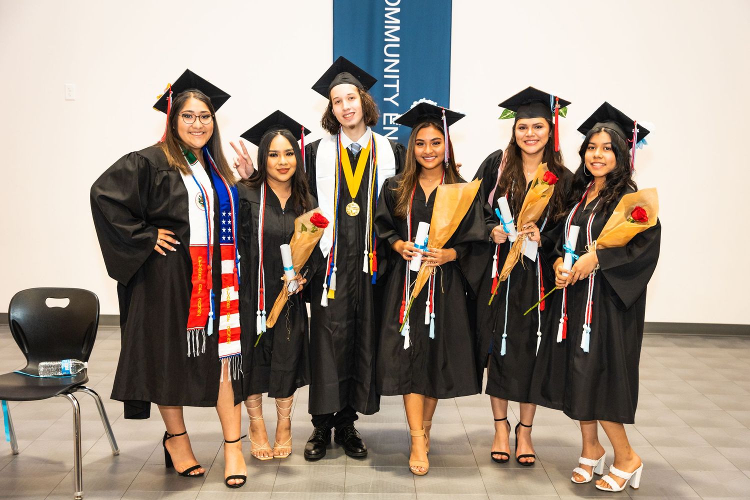 Group of graduates in caps and gowns posing with honors cords and stoles at commencement.