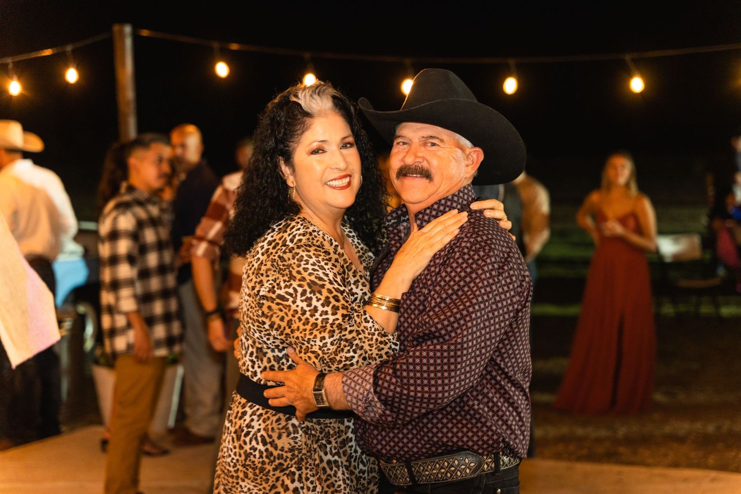 A couple dancing together at a country western themed wedding reception under string lights.