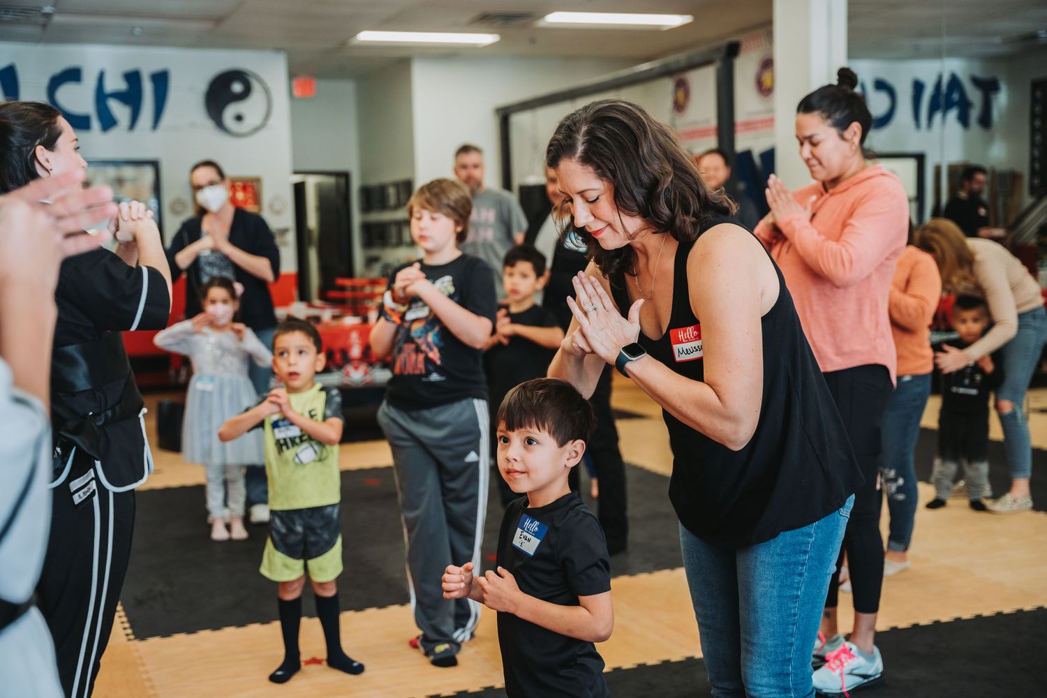 Students and instructors practicing martial arts techniques in a studio with yin yang symbol on wall.