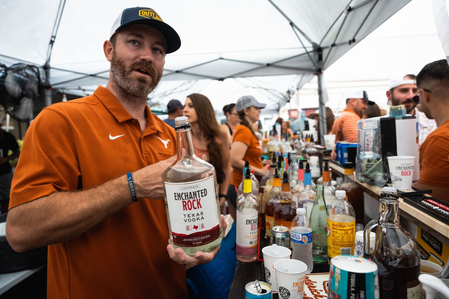 Bartender showcases bottle of liquor while working outdoor festival bar.