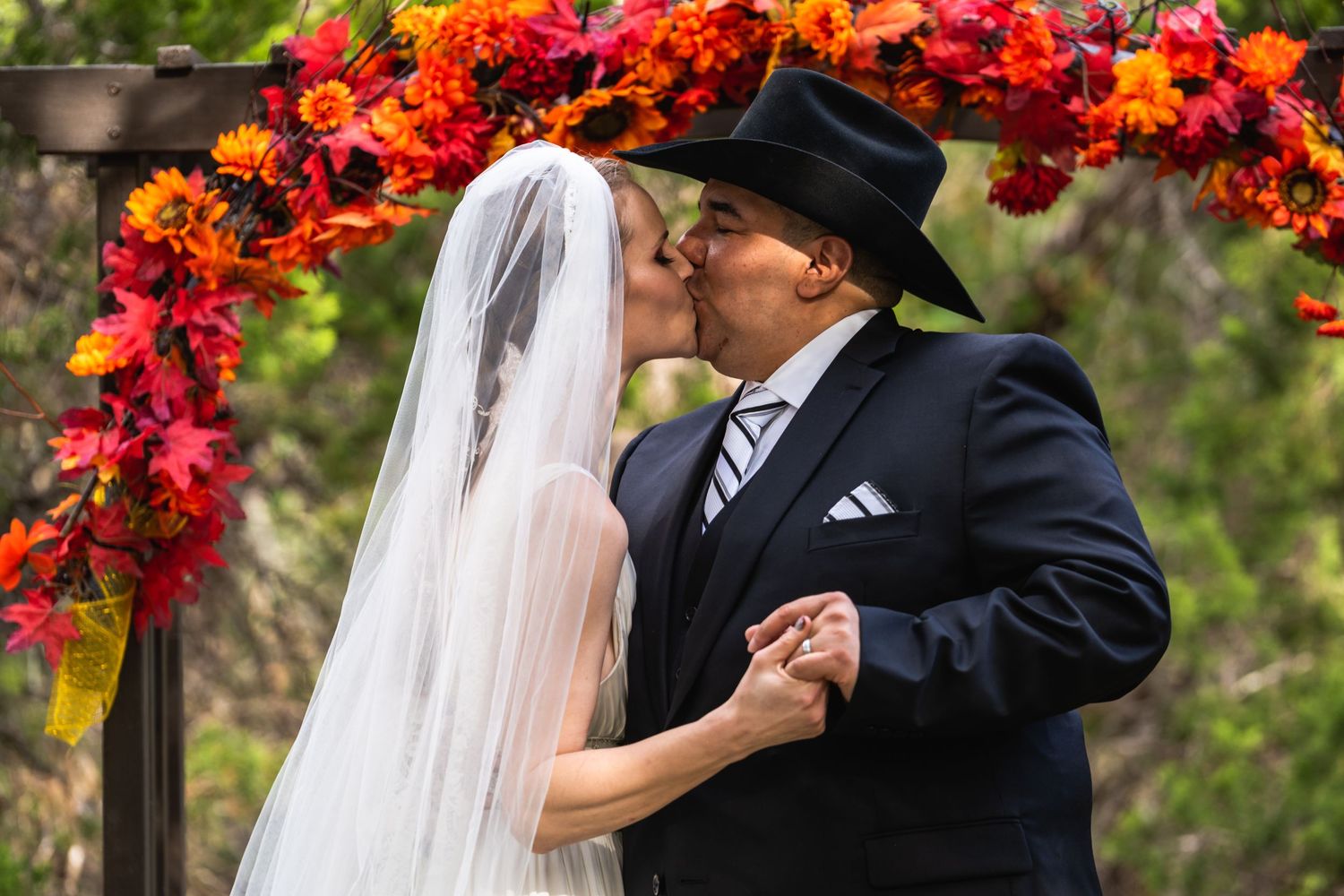 A romantic kiss shared under a stunning red and orange floral wedding arch.