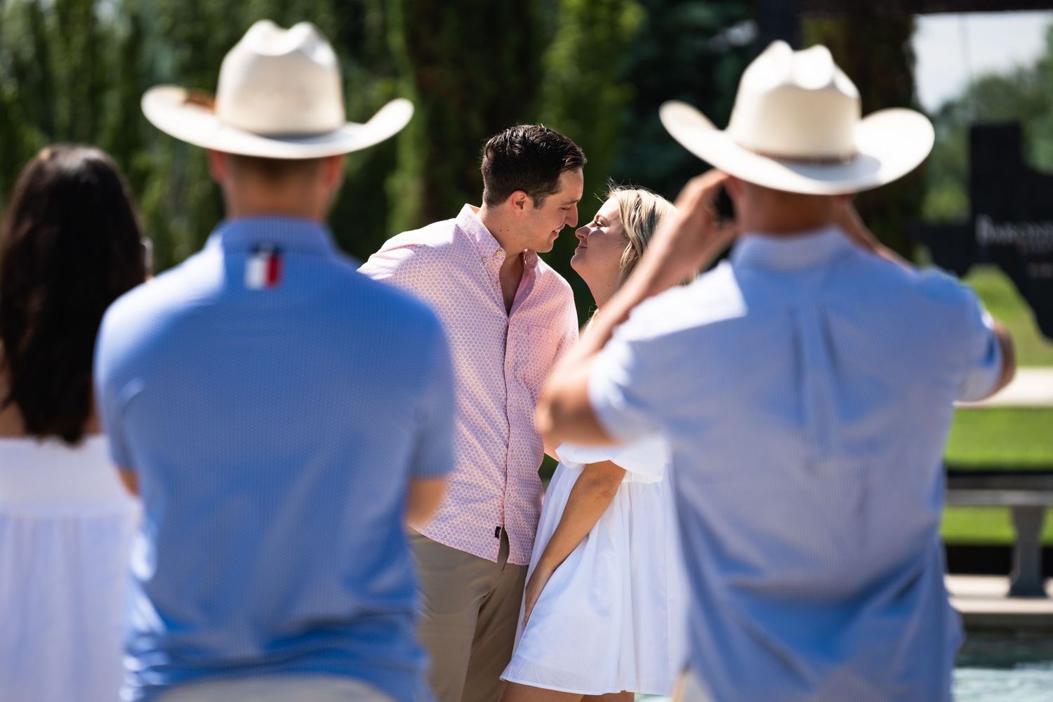 Two people in cowboy hats watch a romantic moment at an outdoor wedding ceremony.